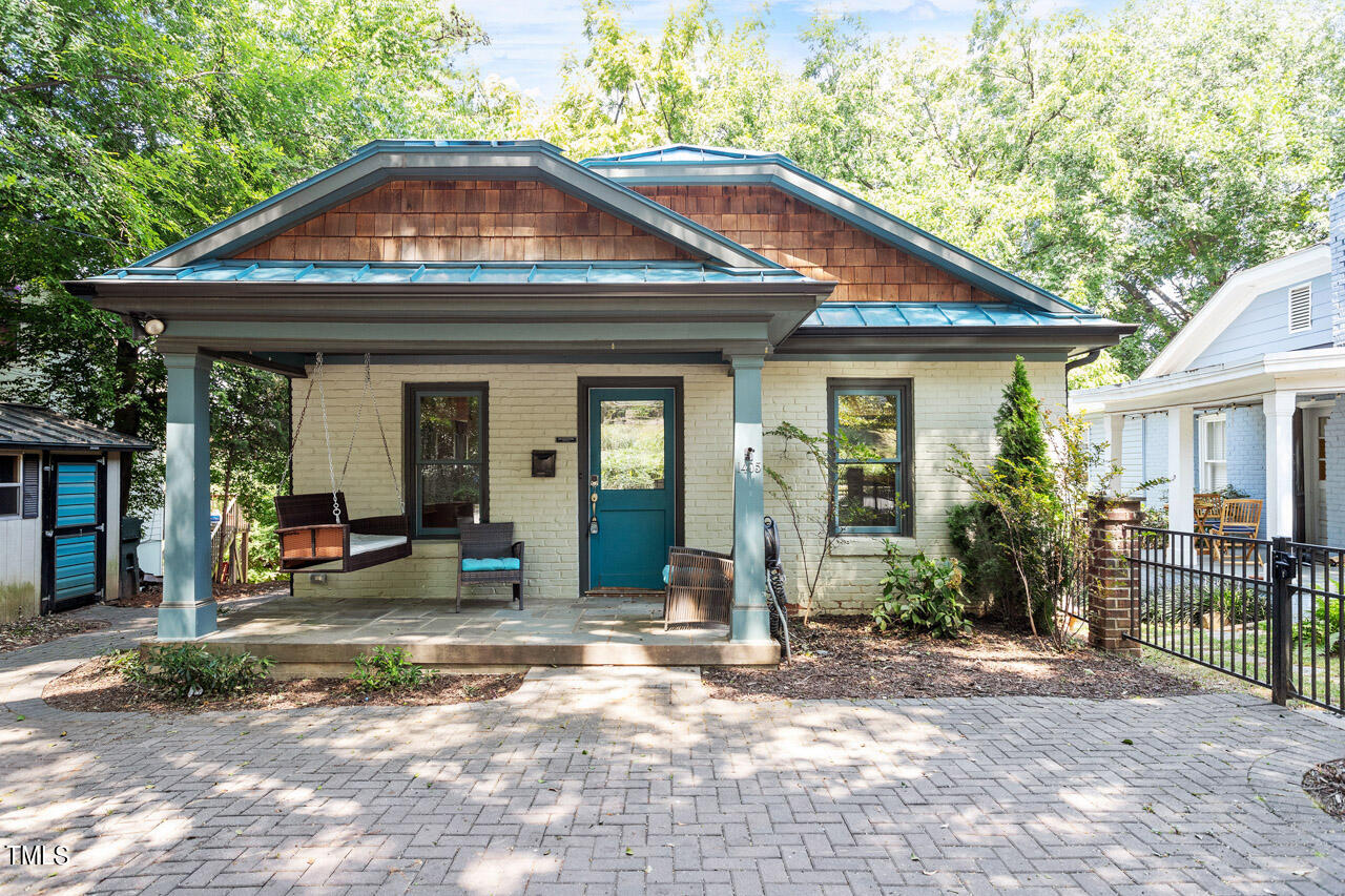 Brick house with a teal door, copper-toned roof, and covered porch with a hanging swing.