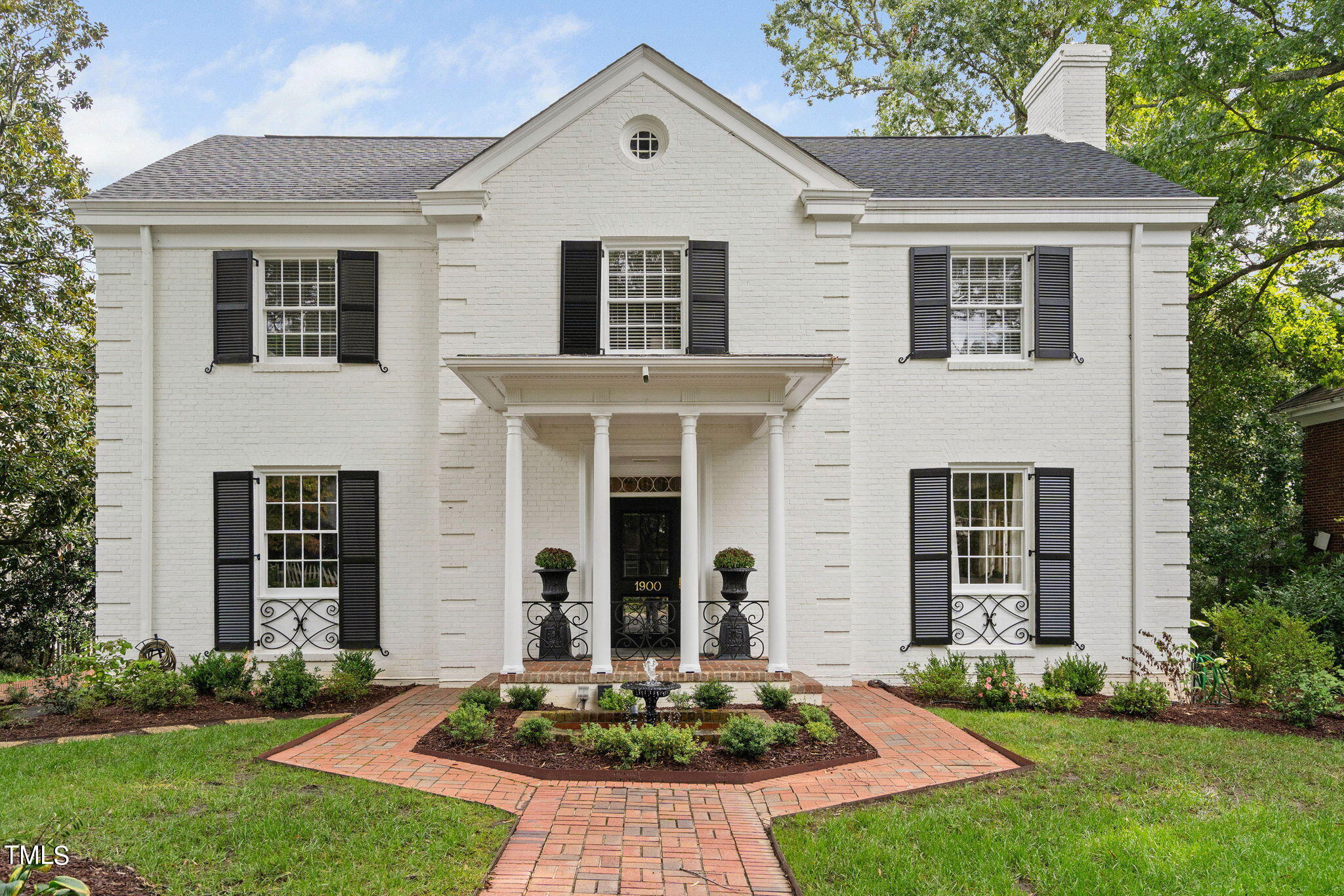 White brick house with black shutters, columned entrance, and landscaped brick walkway.