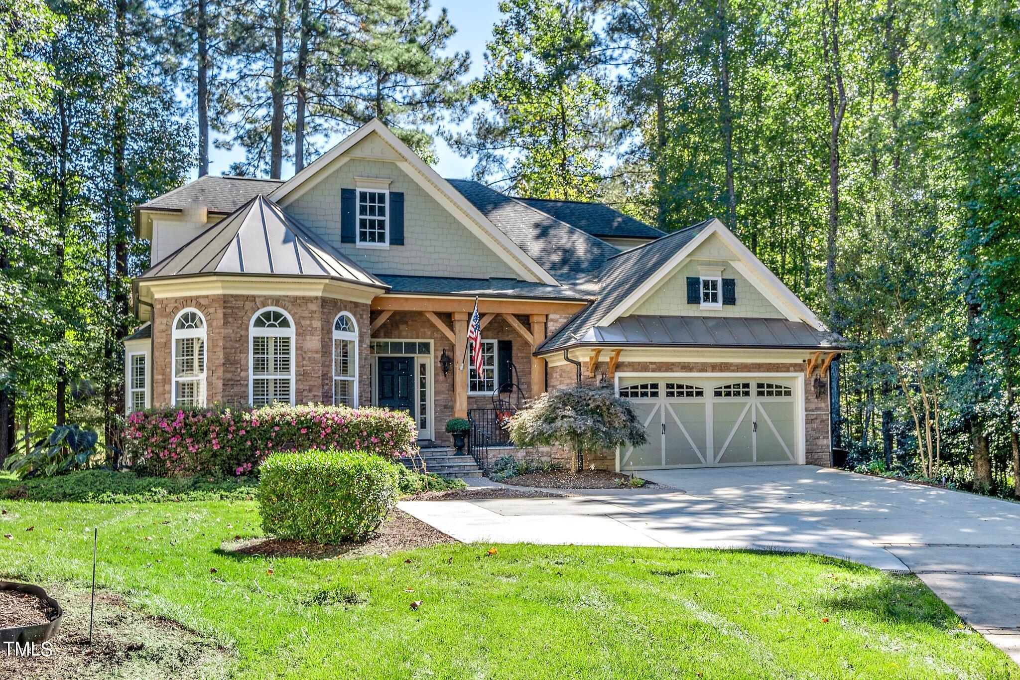 Two-story stone-and-shingle home with a covered entry, double garage, and landscaped lawn beneath mature trees.