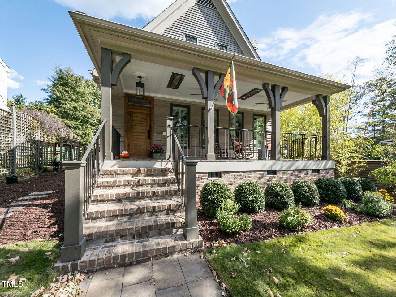 Home with a spacious covered front porch, brick steps, dark railings, and landscaped shrubs.