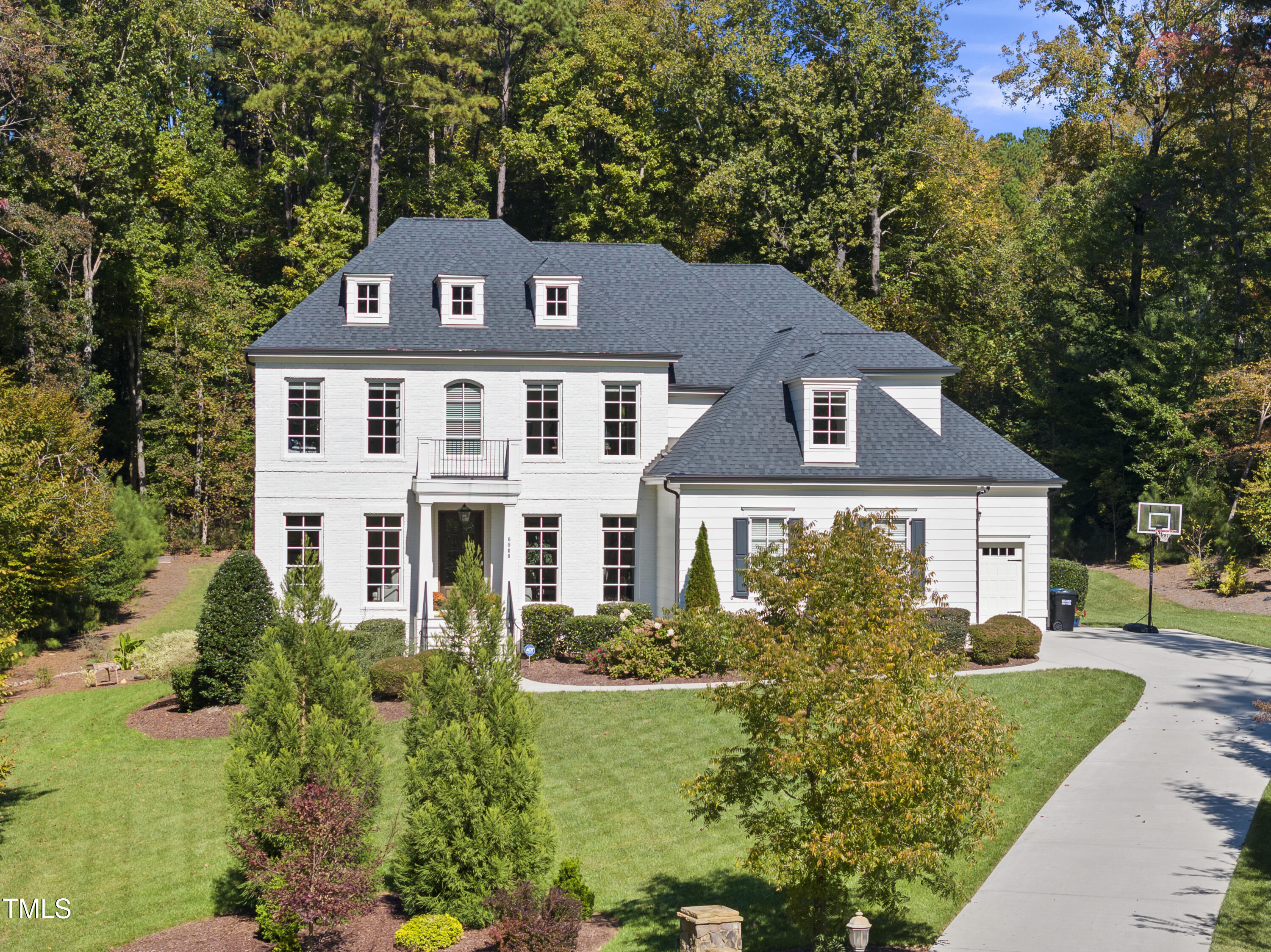White two-story home with gabled roof, landscaped lawn, attached garage, and basketball hoop.