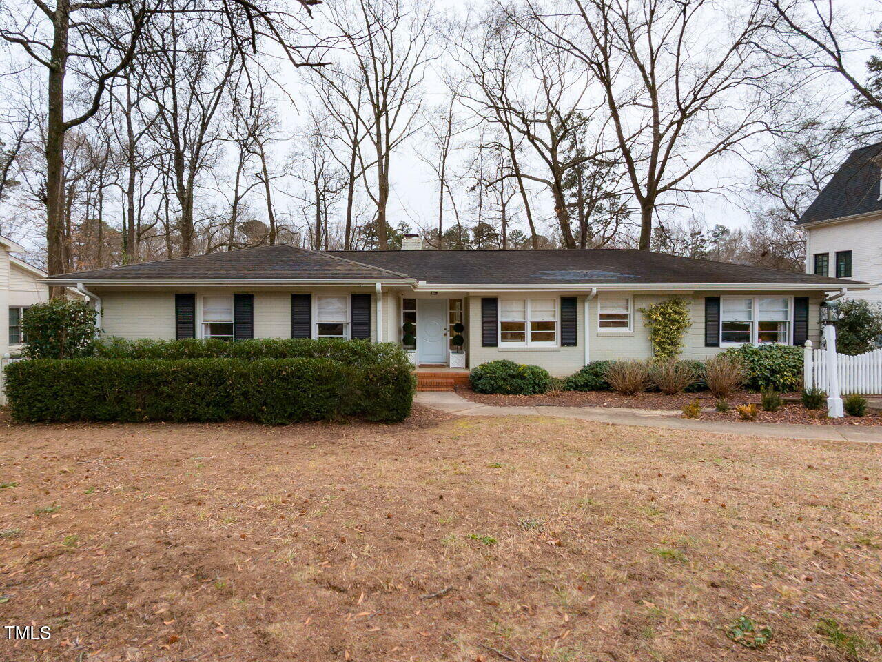 Single-story home with light siding and dark shutters, framed by leafless trees and a broad lawn.