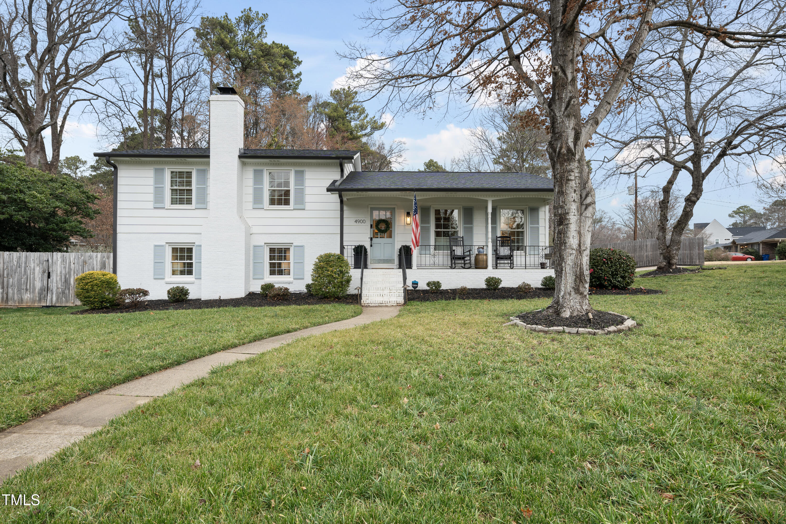 White two-story home with a covered porch, pale blue shutters, and a curved front walkway beneath large bare trees.