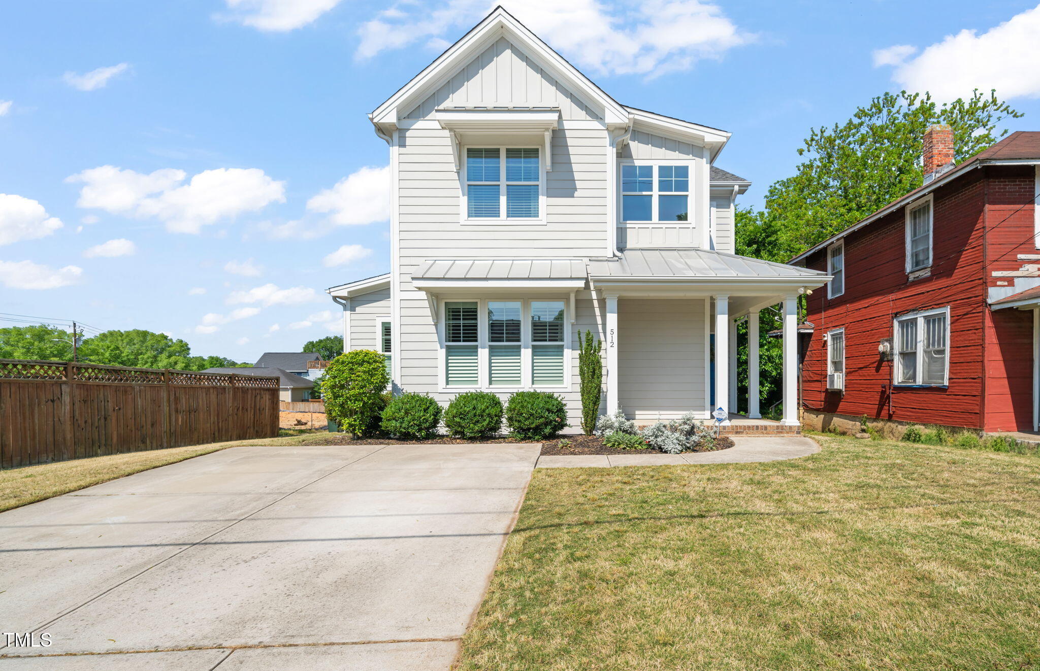 White two-story house with covered porch and wide driveway, next to a red house.