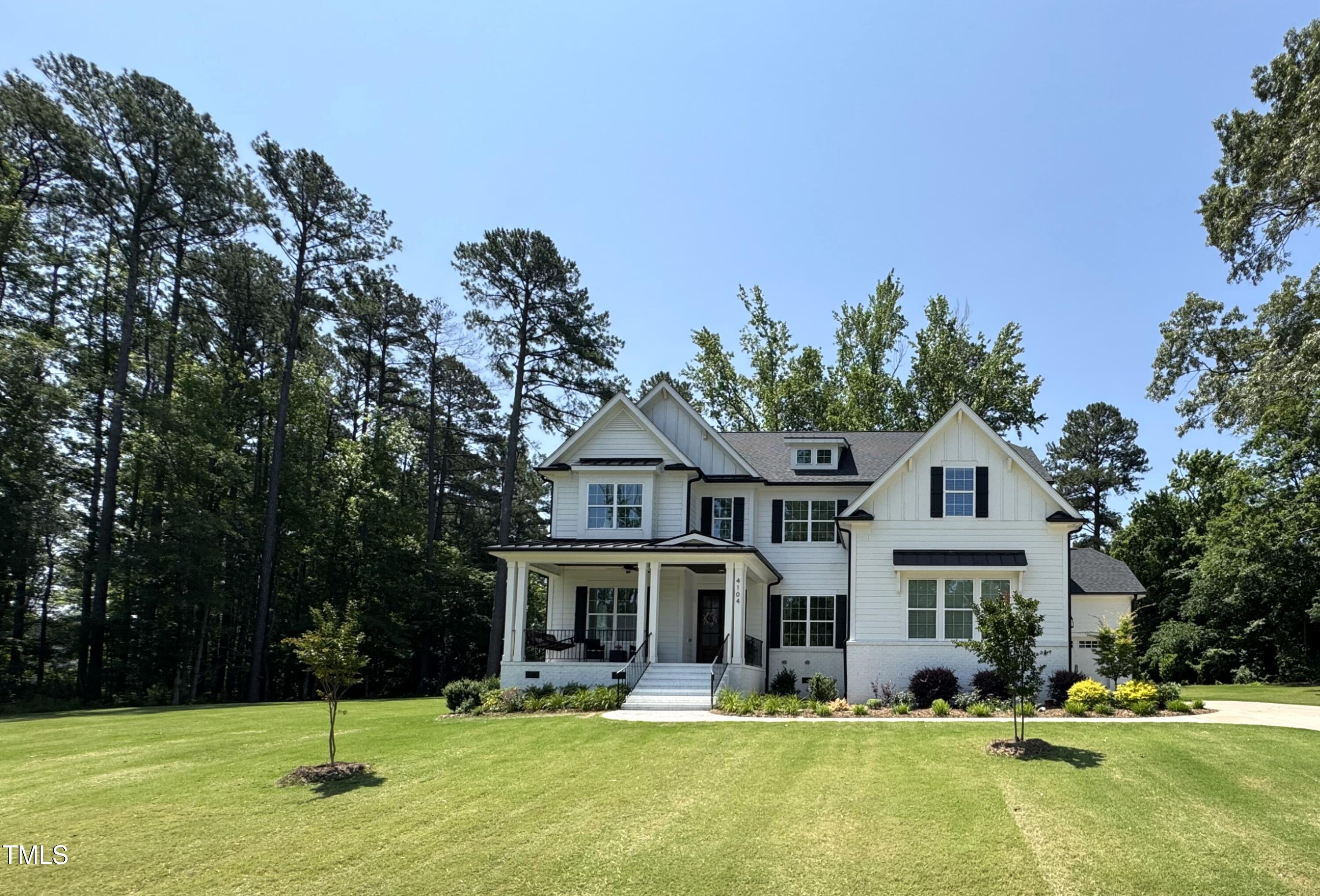 White two-story house with black shutters and a covered porch, set behind a broad lawn and mature trees.