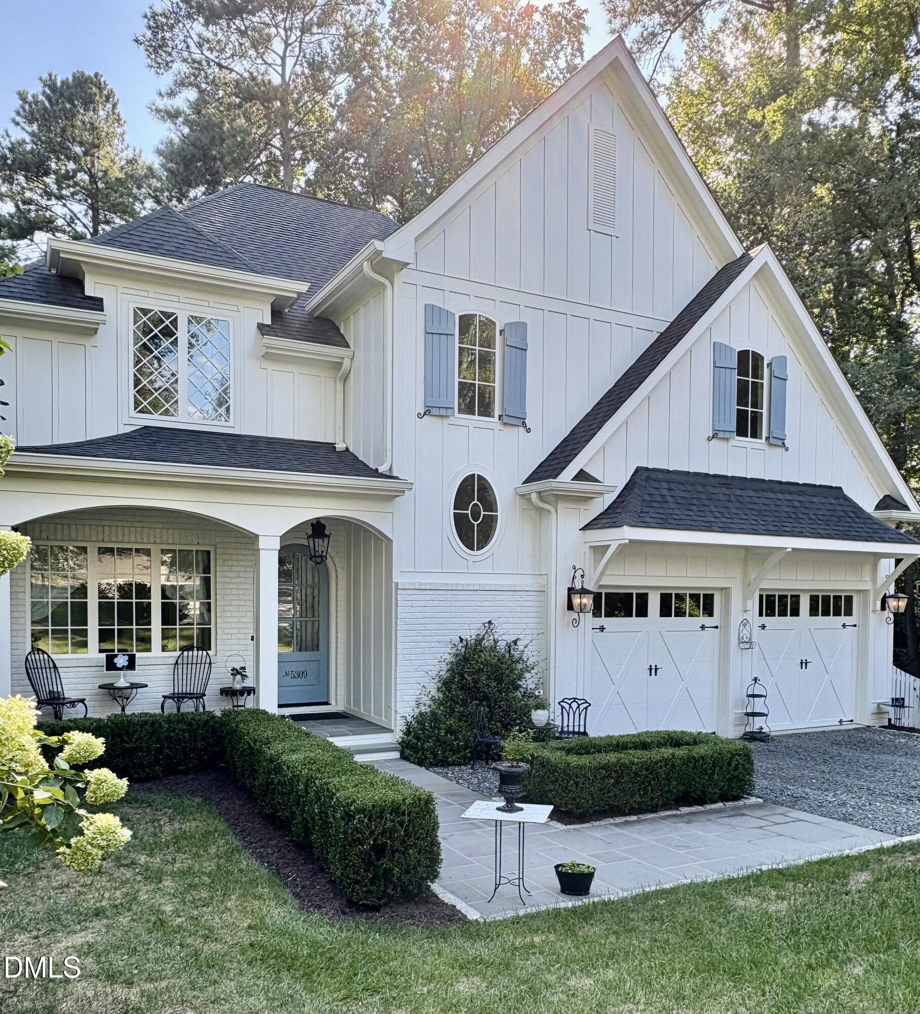 White two-story home with blue shutters, a double garage, and landscaped front patio.