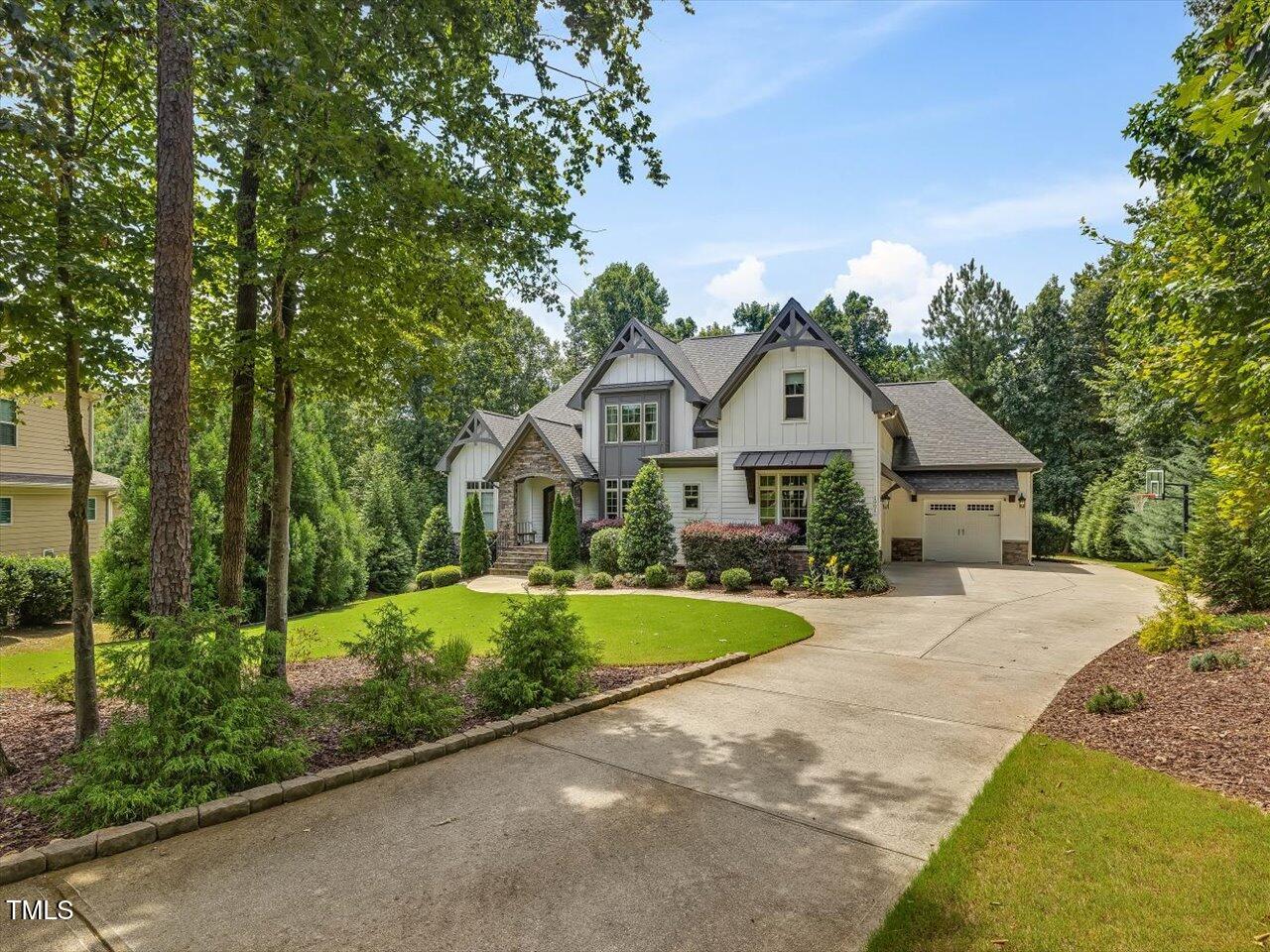 White gabled home with stone accents, attached garage, mature trees, and a curved driveway.