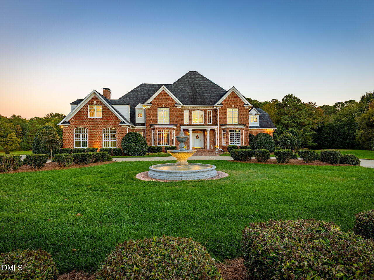 Red-brick house with a central fountain, manicured lawn, and clipped shrubs.