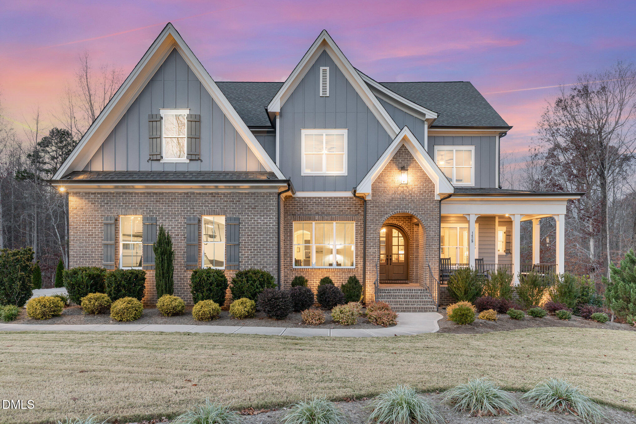 Two-story gray-and-brick home with steep gables and a warmly lit covered porch at dusk.