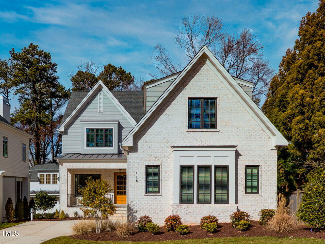 White brick house with steep gables, dark-framed windows, and a landscaped front yard.