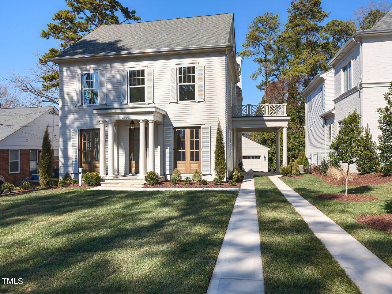 White two-story house with a columned porch, landscaped lawn, and covered passage between neighboring buildings.