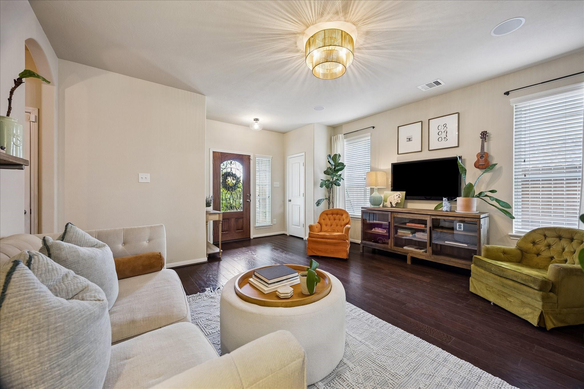 Staged living room with dark wood floors, colorful armchairs, and an ornate glass-panel entry door.