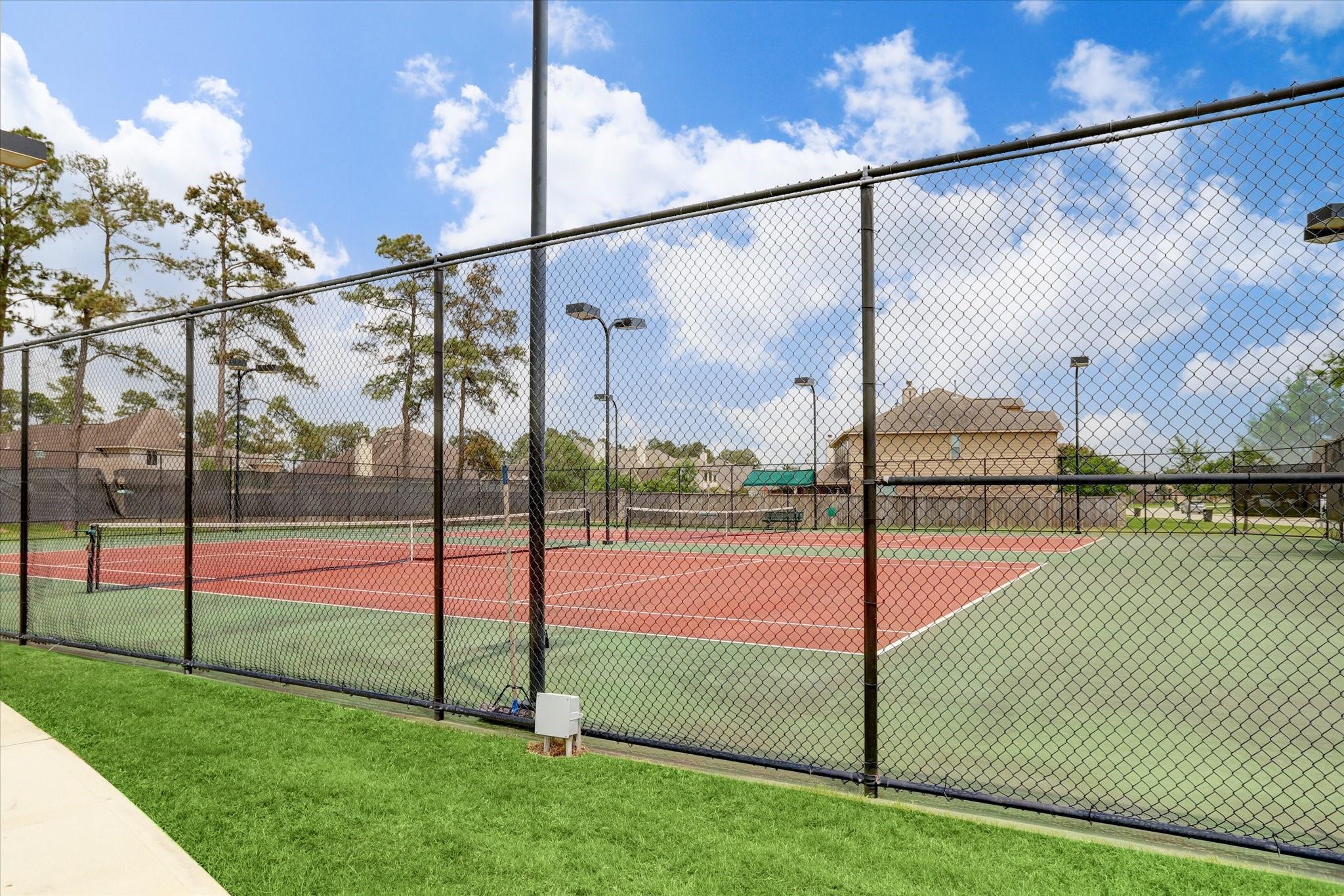 Fenced outdoor tennis courts with red and green surfaces and nearby homes.