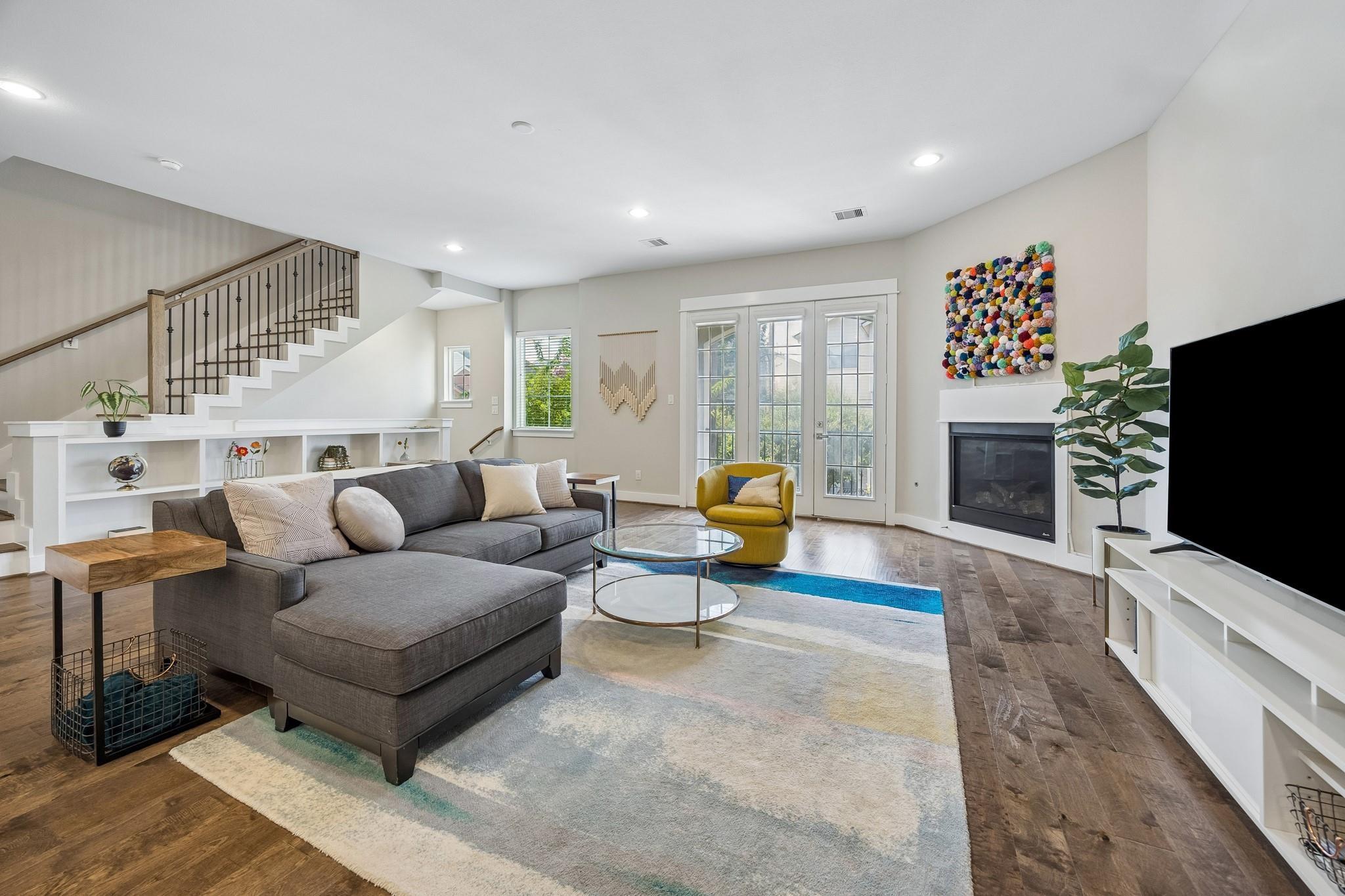 Staged living room with a gray sectional, staircase, French doors, and fireplace.