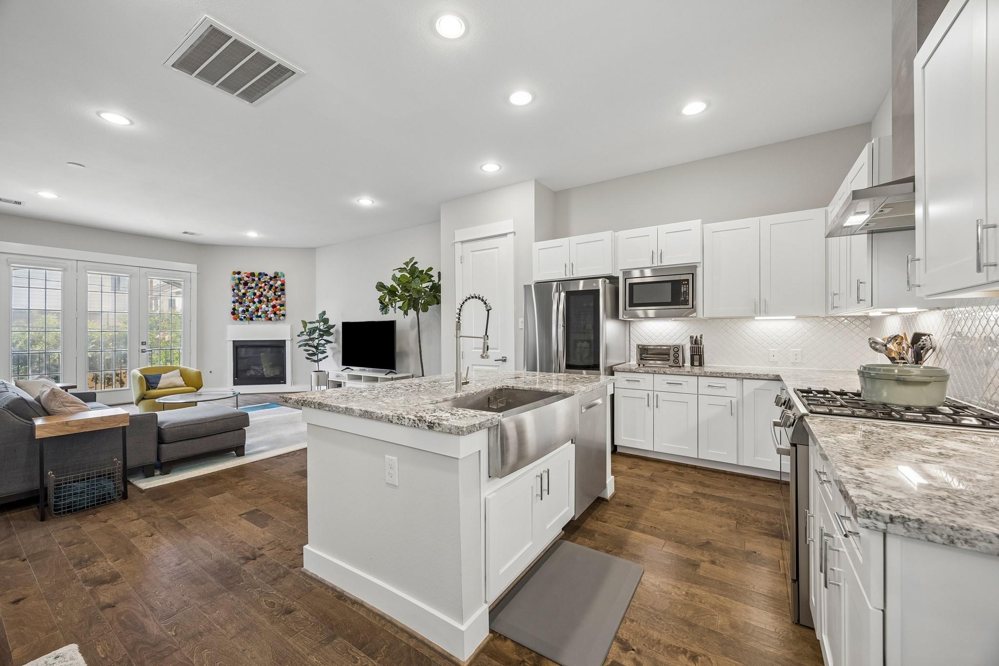 Open-plan kitchen with a large farmhouse-sink island, white cabinetry, and adjoining living room.