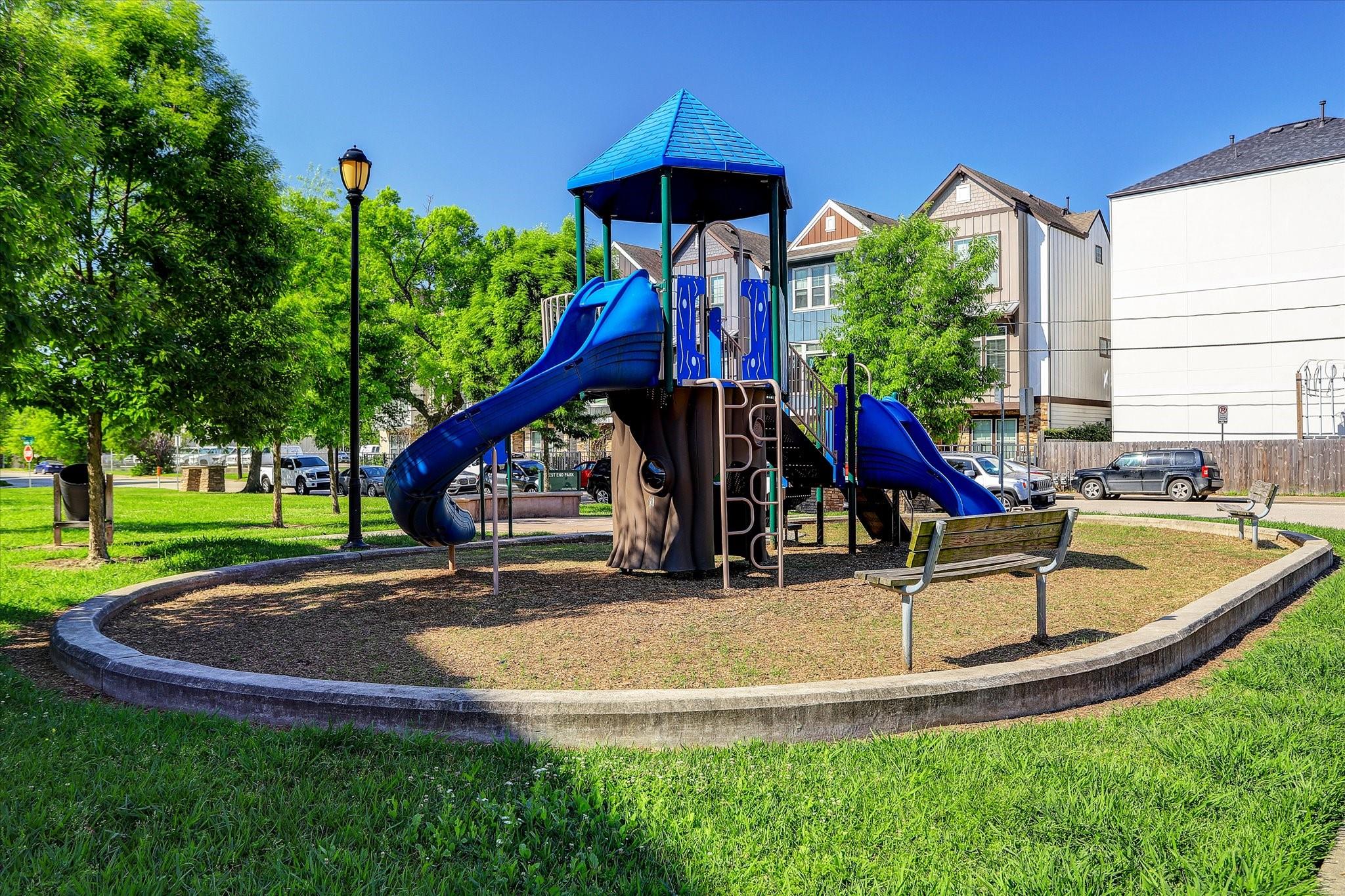 Neighborhood playground with a blue-roofed play structure, twin slides, and a wooden bench.