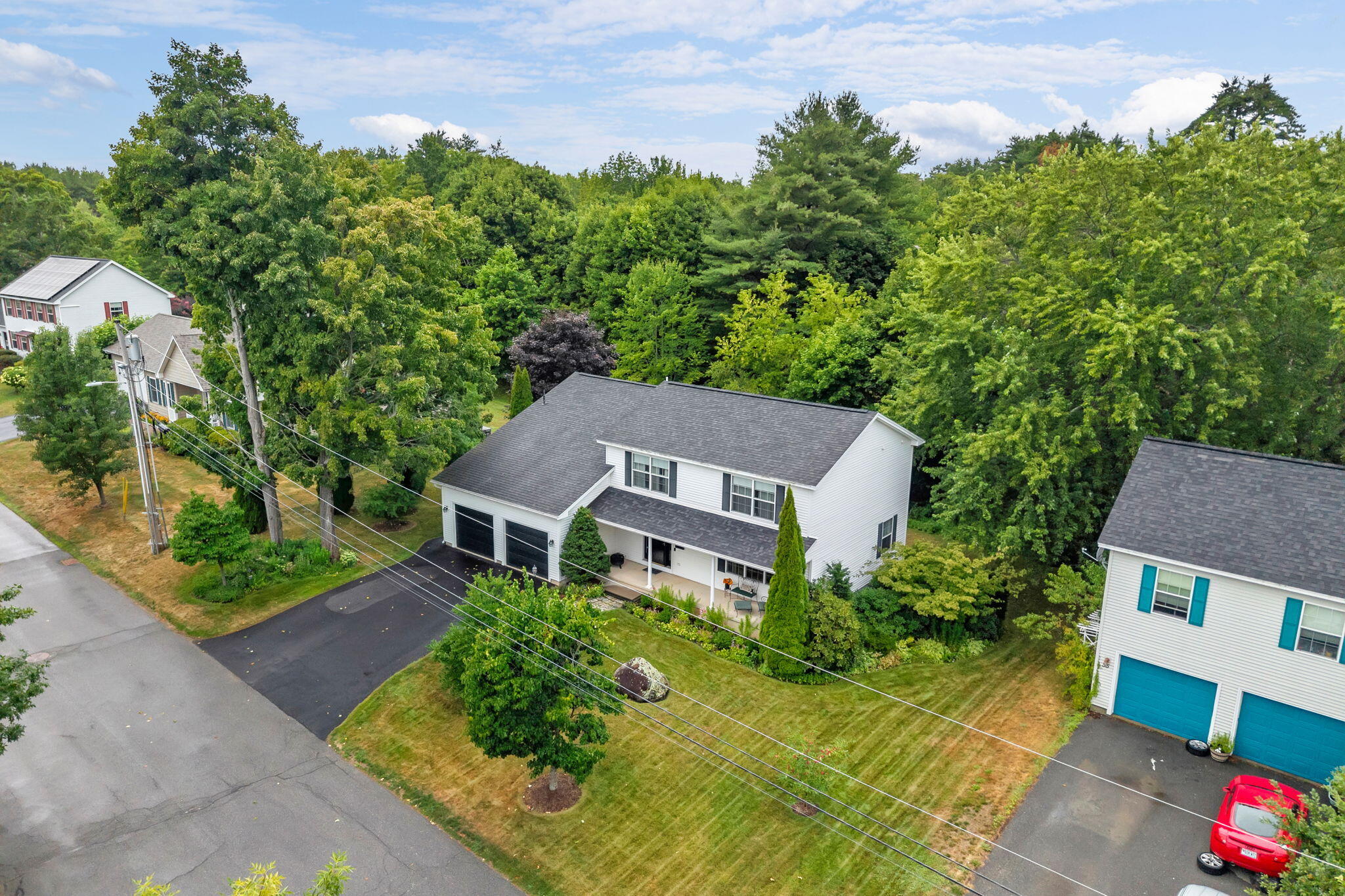 Aerial view of a white two-story house with an attached garage, driveway, and tree-lined yard.