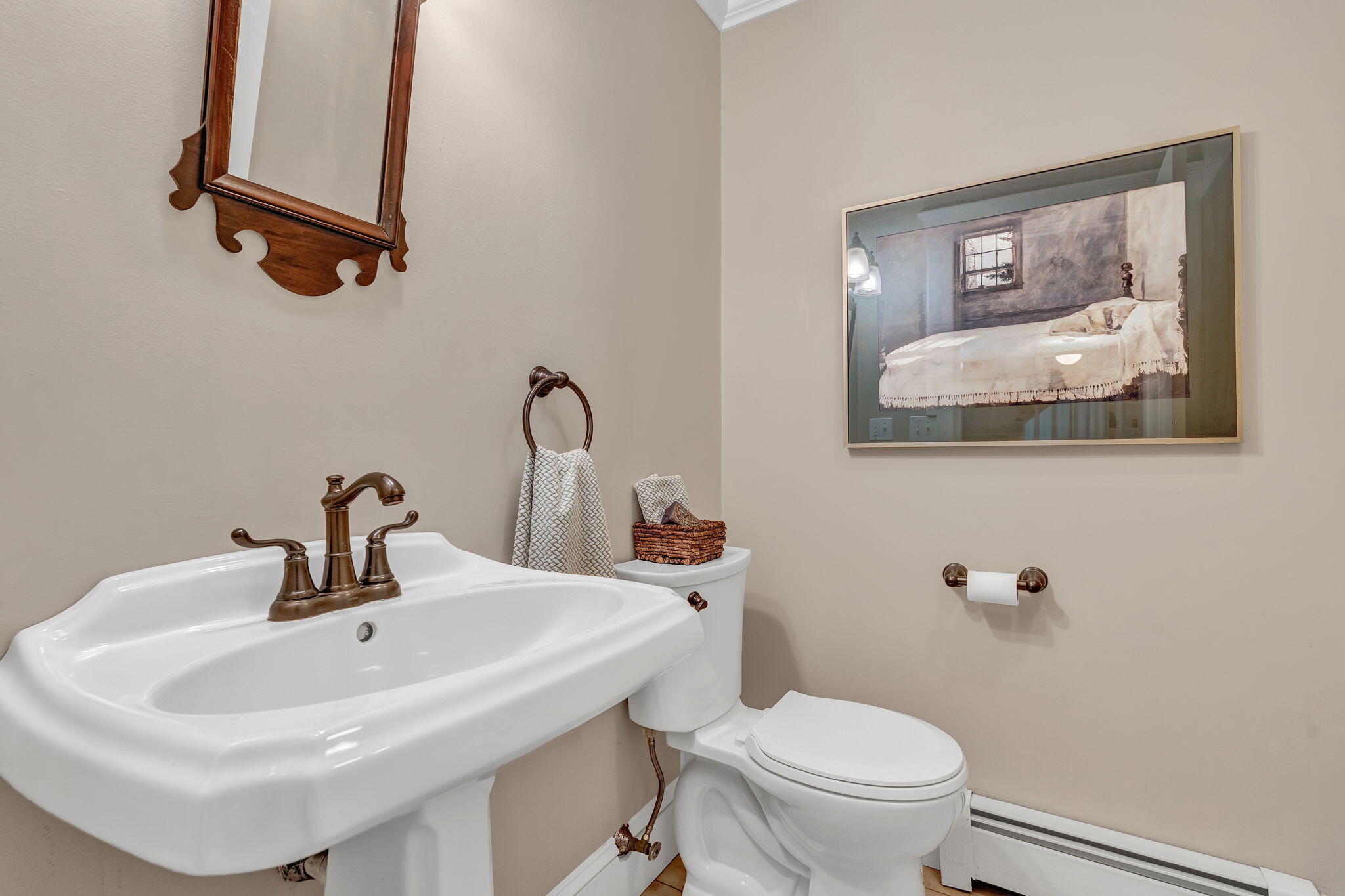 Bathroom with a pedestal sink, bronze fixtures, and framed artwork above the toilet.
