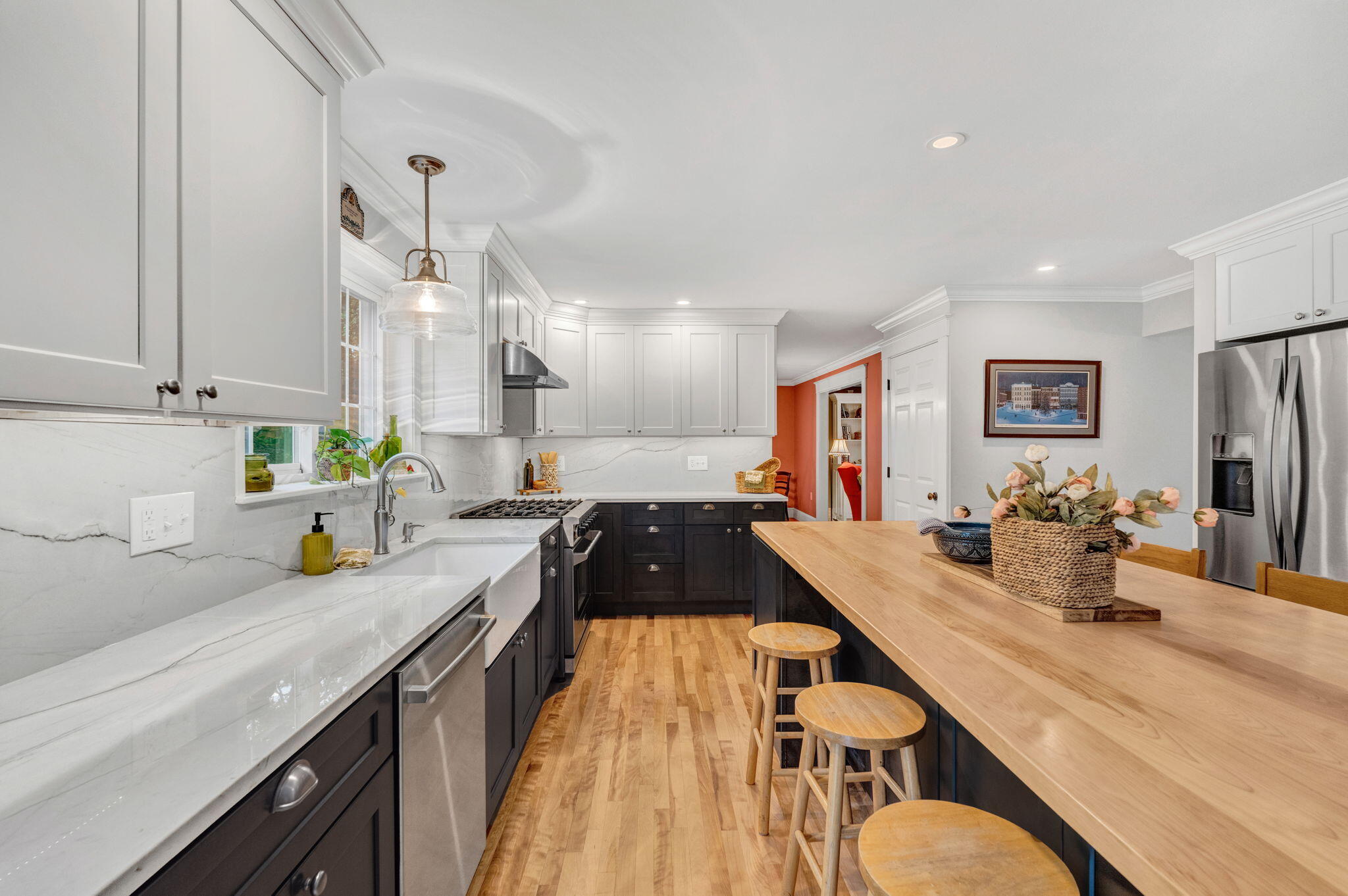Kitchen with a long wood island and stools, white cabinets, dark lower cabinets, and marble-look counters.