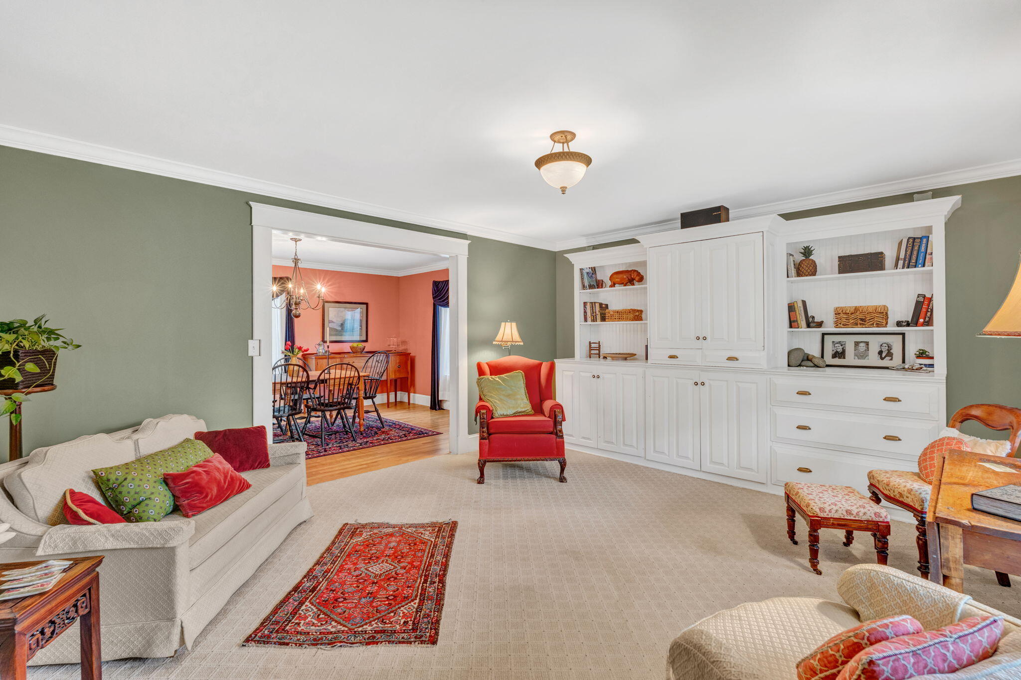 Living room with white built-in bookshelves, a red armchair, and an adjoining coral dining room.