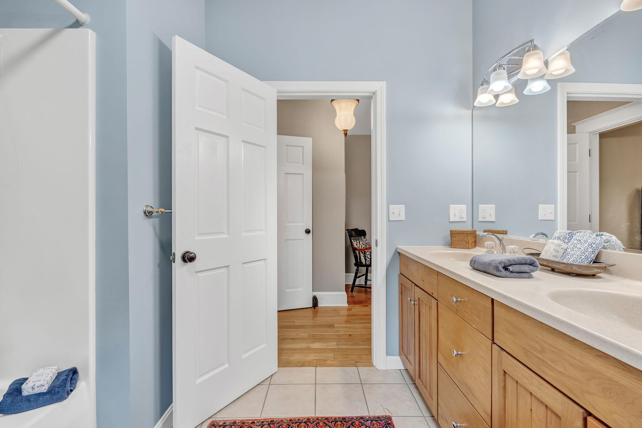 Bathroom with a long wood vanity, double sinks, pale blue walls, and a white bathtub.