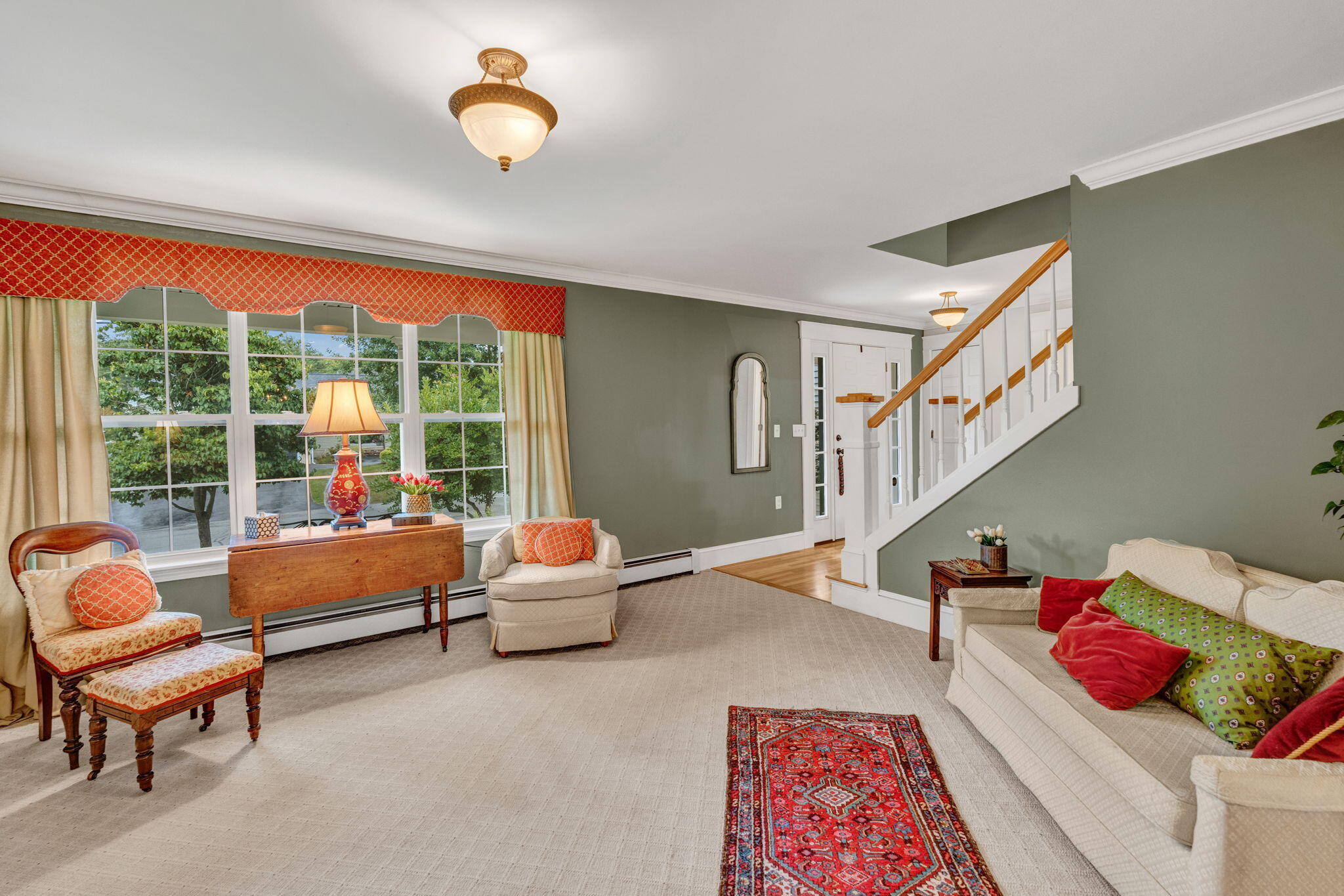 Living room with a large picture window, cream seating, and a staircase with a wood handrail.