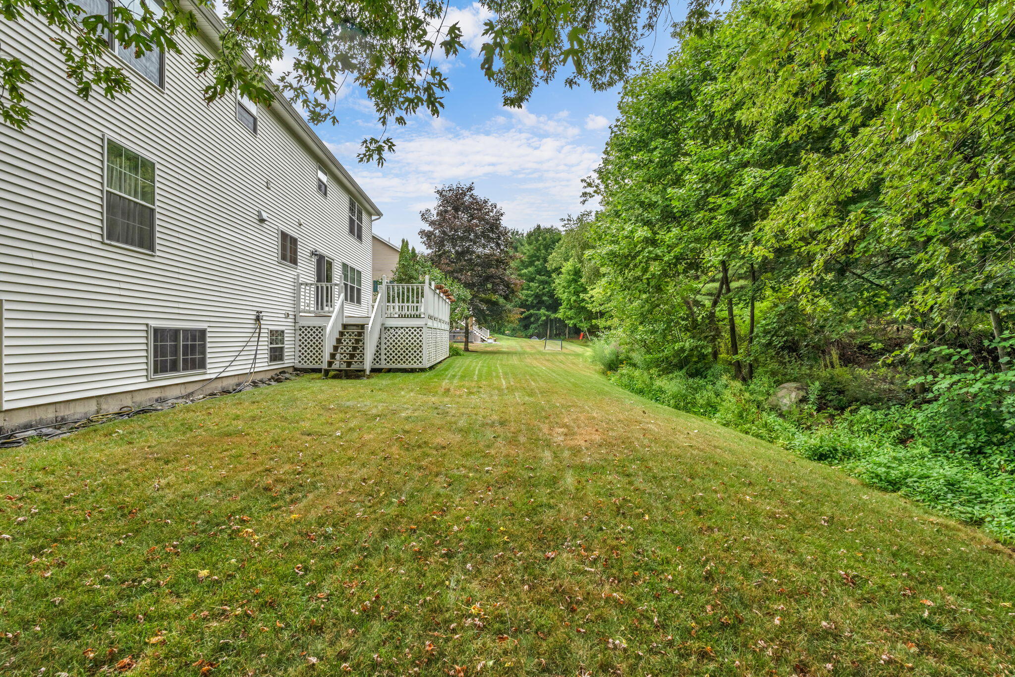 House side yard with a raised deck, broad lawn, and wooded edge.