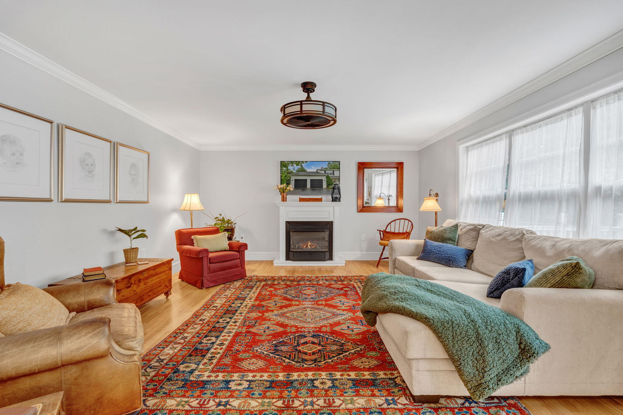 Living room with a white fireplace, large curtained windows, and a vivid patterned rug.