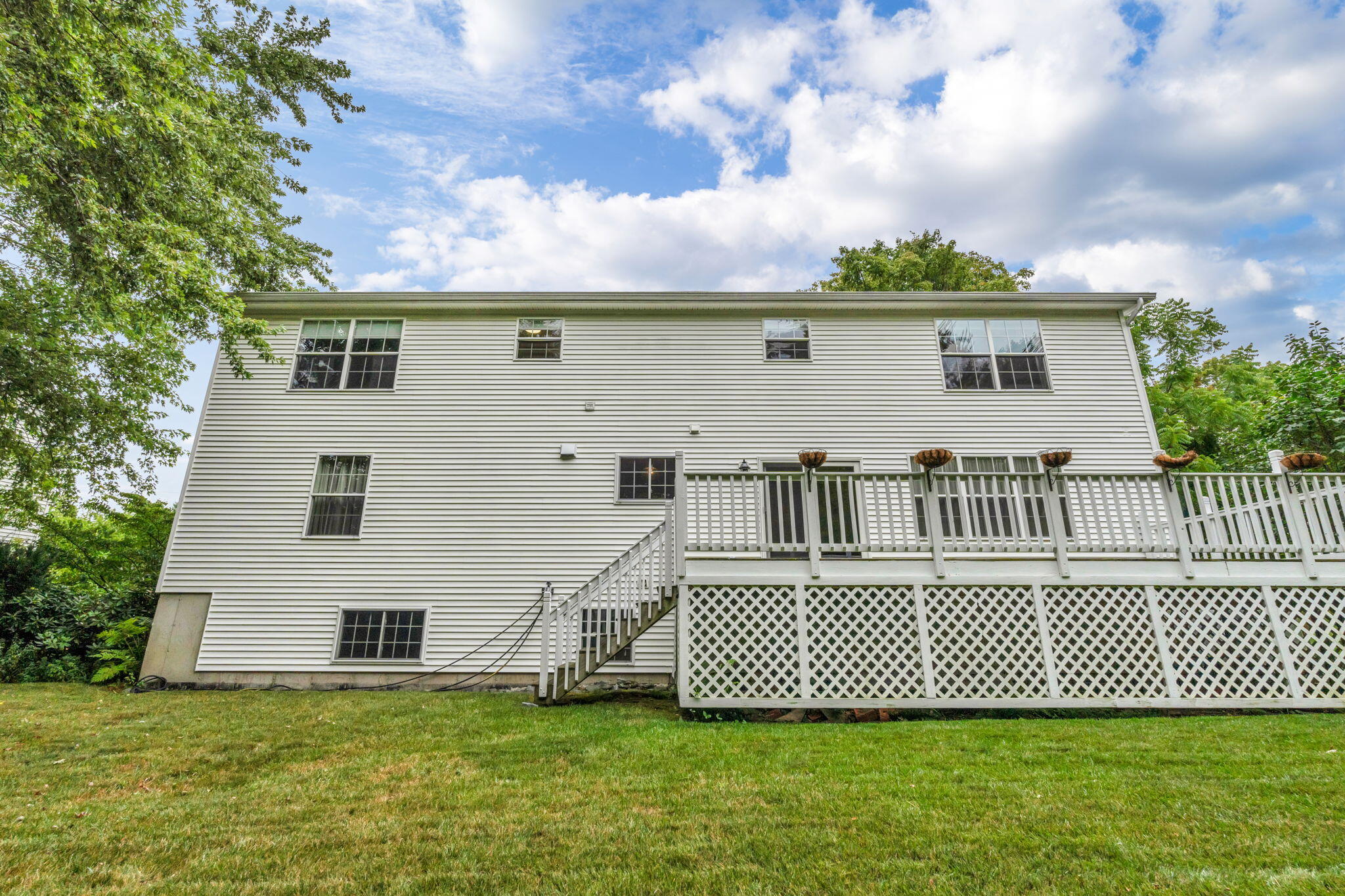 Two-story home's rear exterior with a raised white deck, lattice skirting, and lawn.
