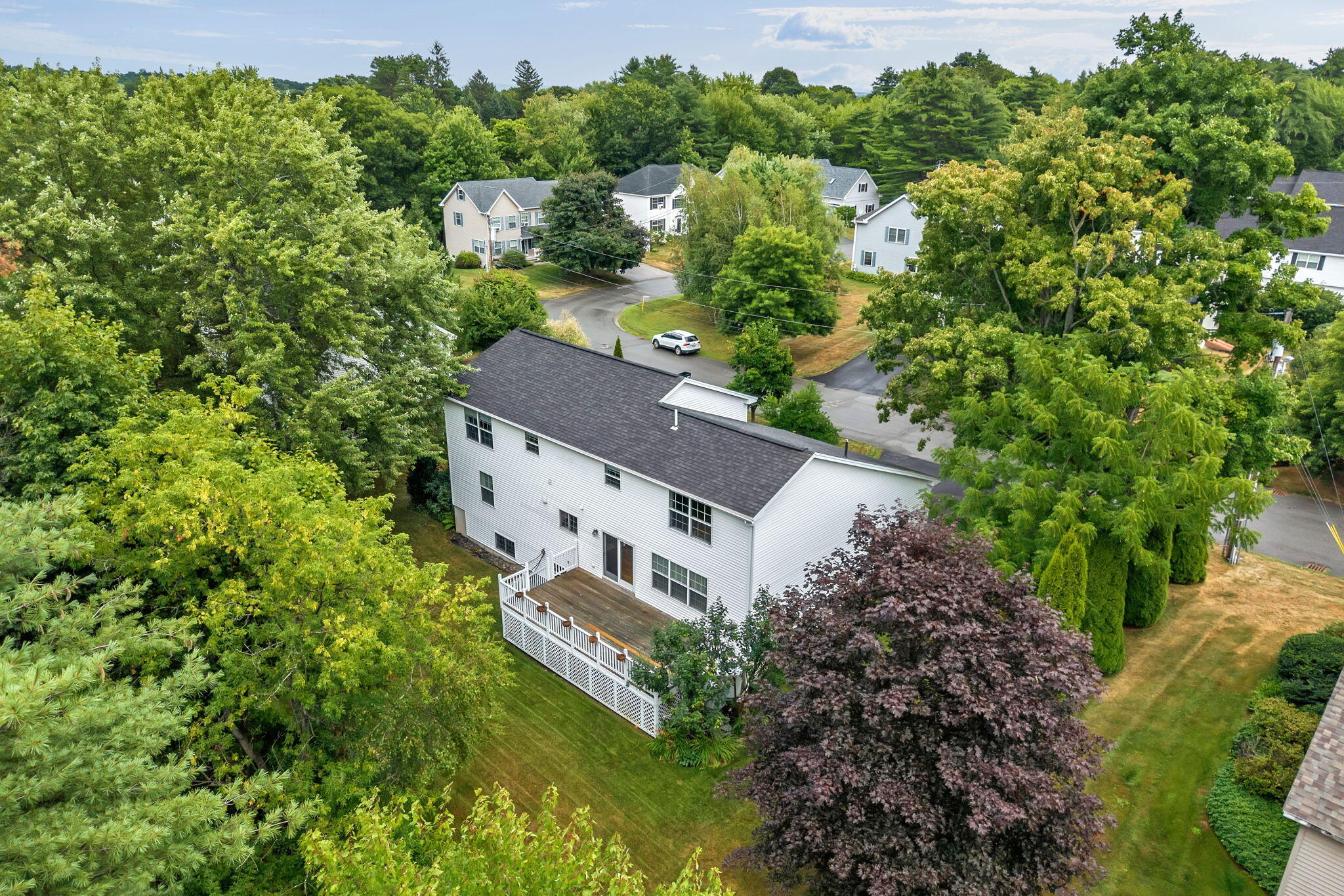 Aerial view of a white two-story home with a large deck, lawn, and mature trees.