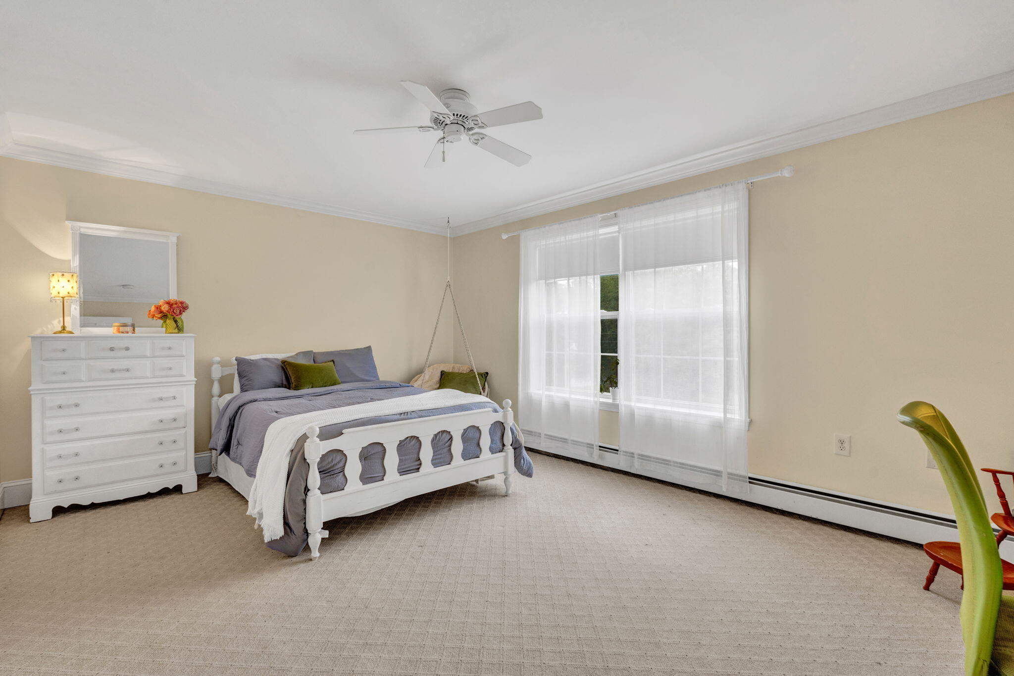 Spacious bedroom with a white bed, gray bedding, white dresser, and large curtained windows.