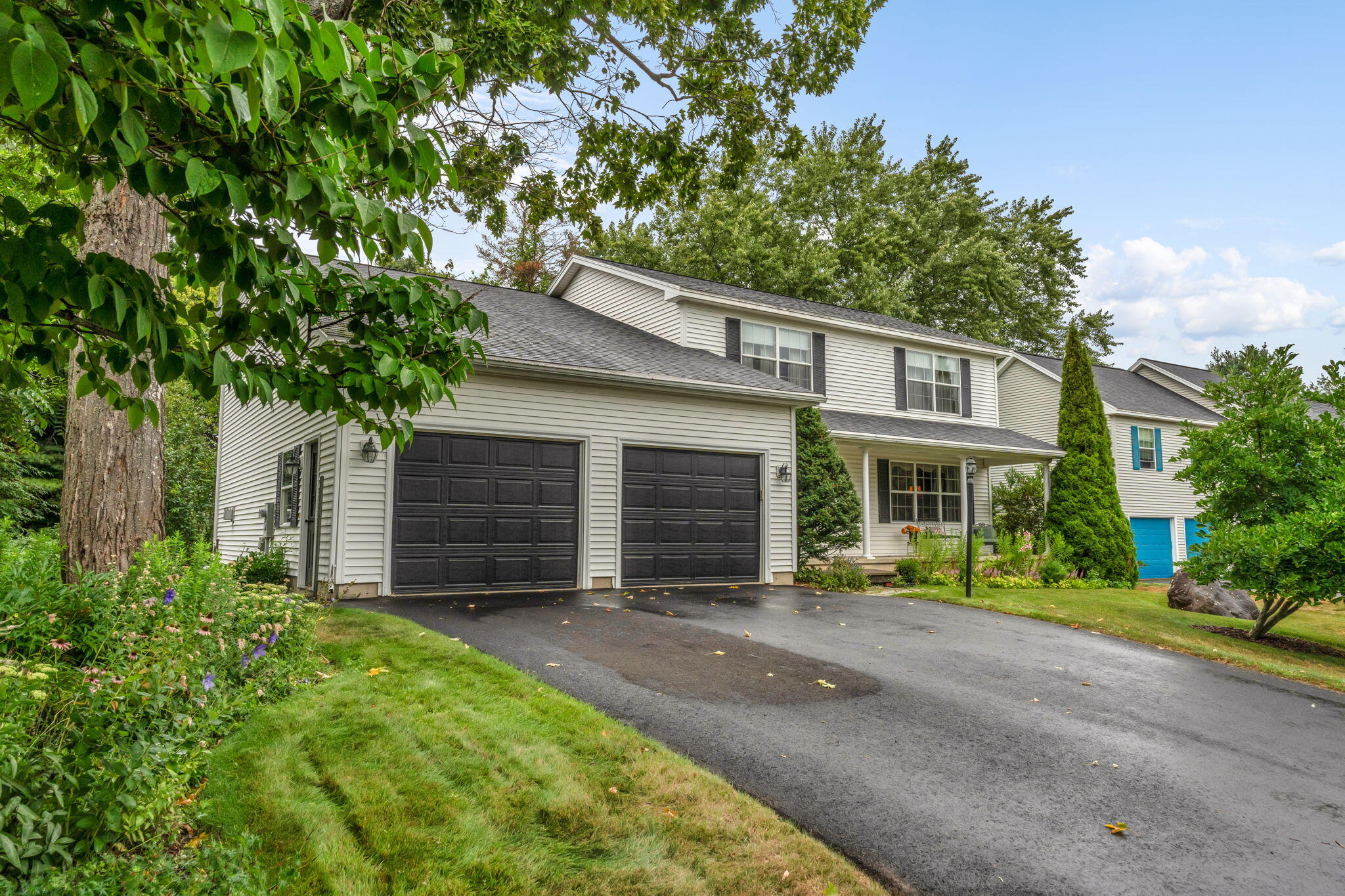 Two-story house with twin dark garage doors, a broad driveway, and mature trees.