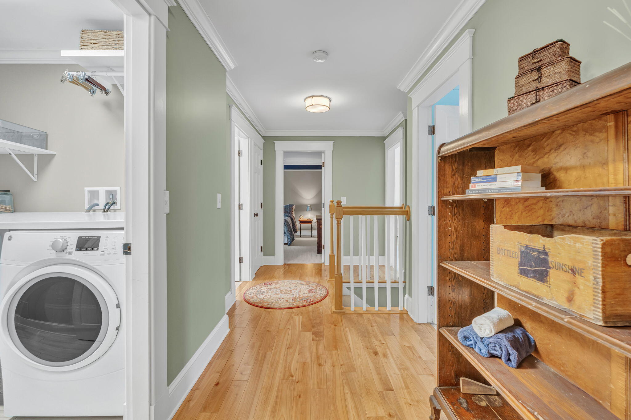 Upstairs hallway with hardwood floors, a laundry nook, and a wooden bookcase beside the stair railing.