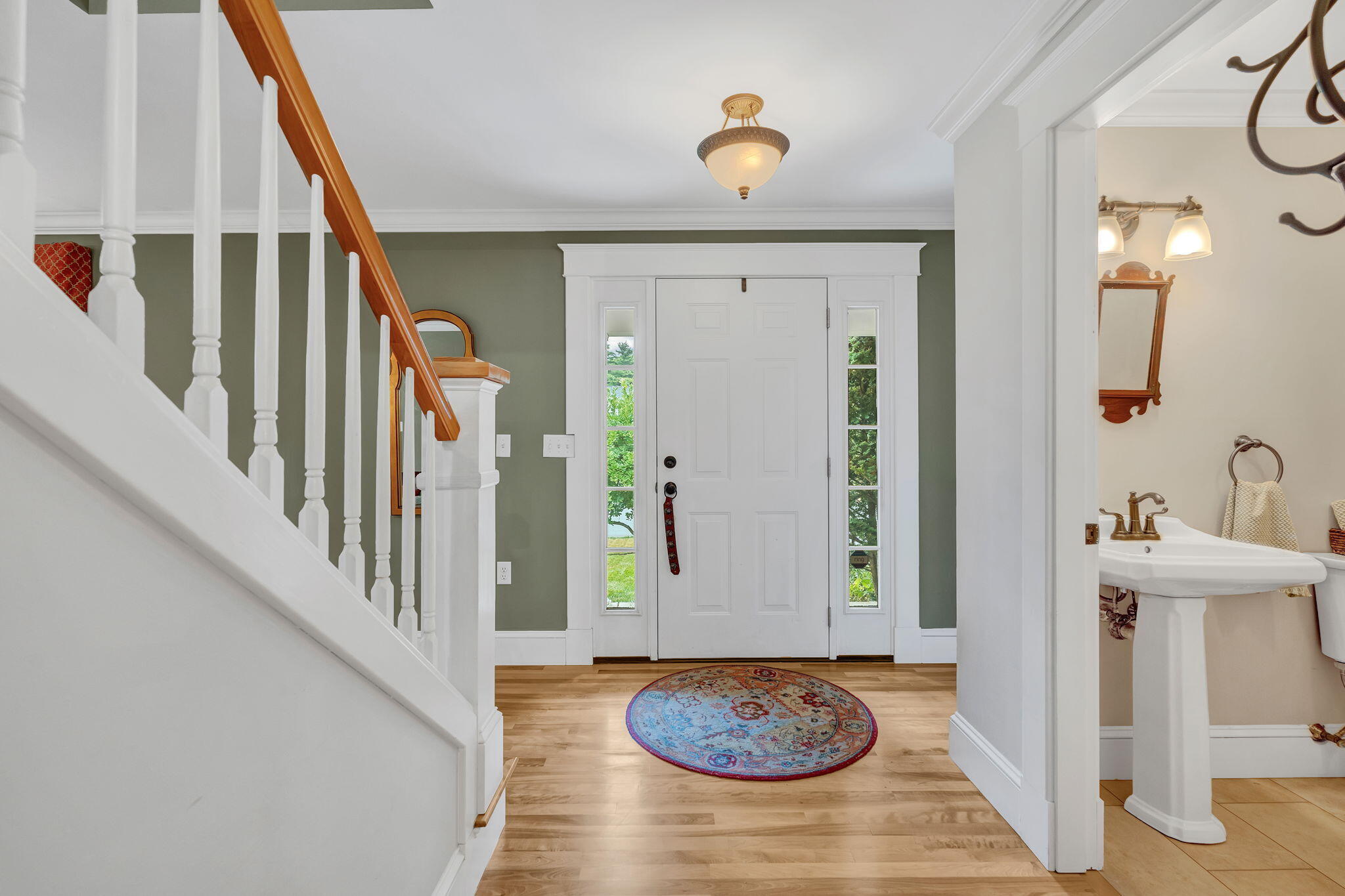 Foyer with an oak staircase, glass-sided front door, hardwood floors, and a view into the powder room.