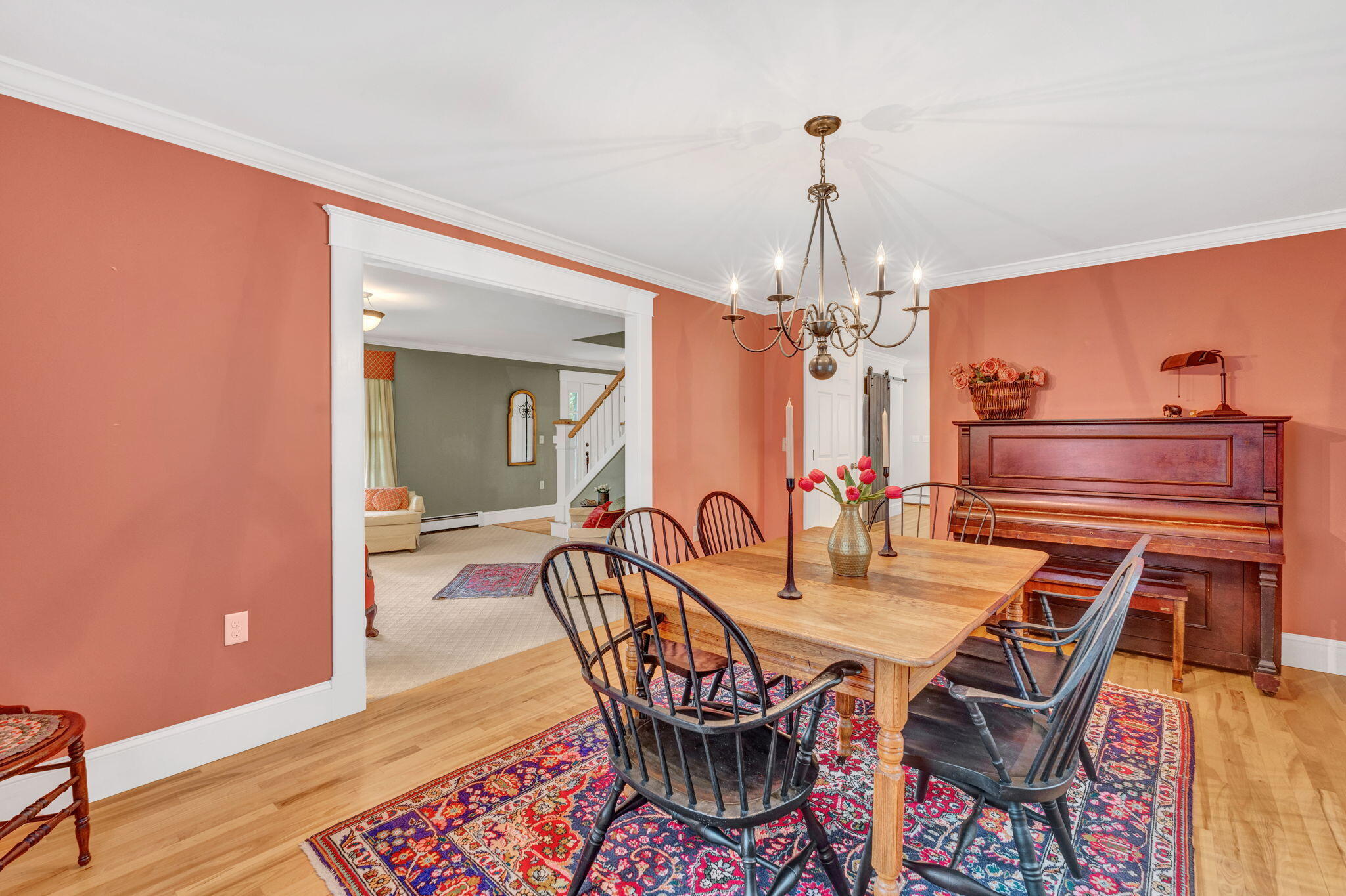 Dining room with salmon walls, a wooden table, chandelier, and upright piano.