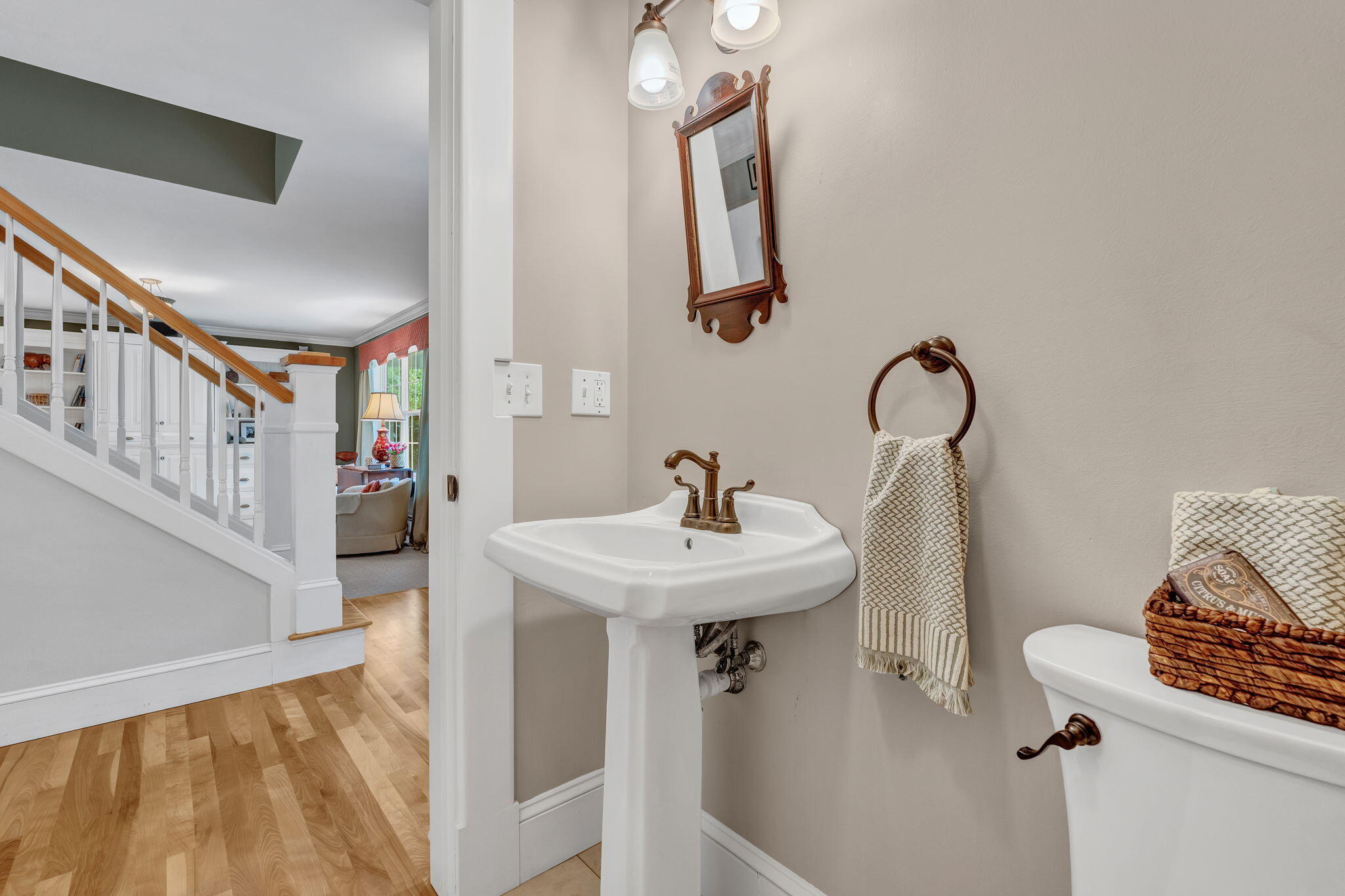 Powder room with a pedestal sink and bronze fixtures beside an open view of the staircase.