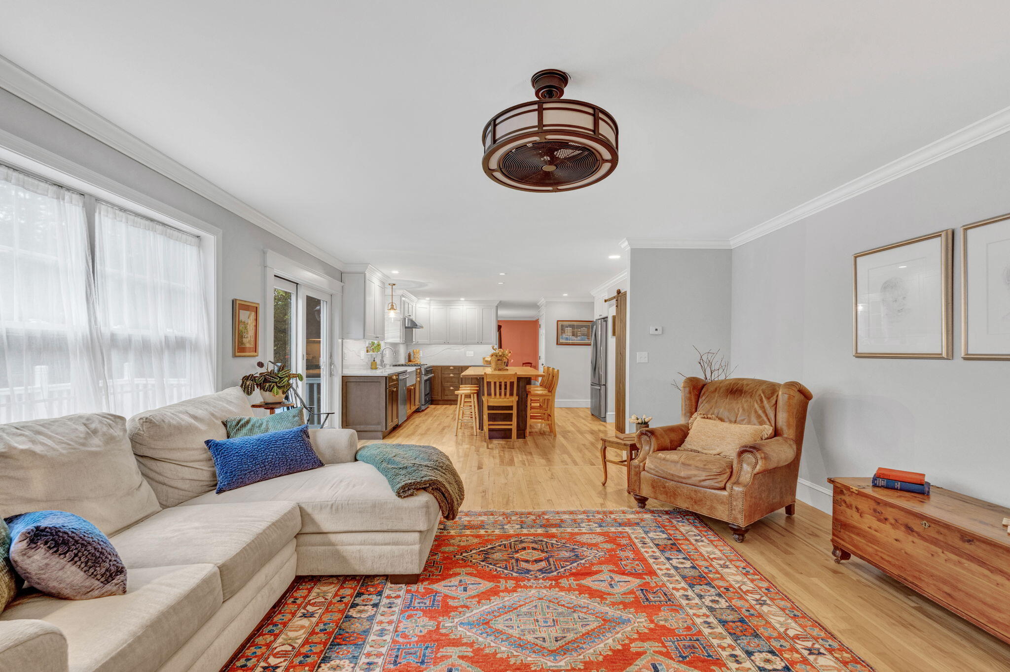 Open-plan living room with a cream sectional, colorful rug, and kitchen and dining area beyond.