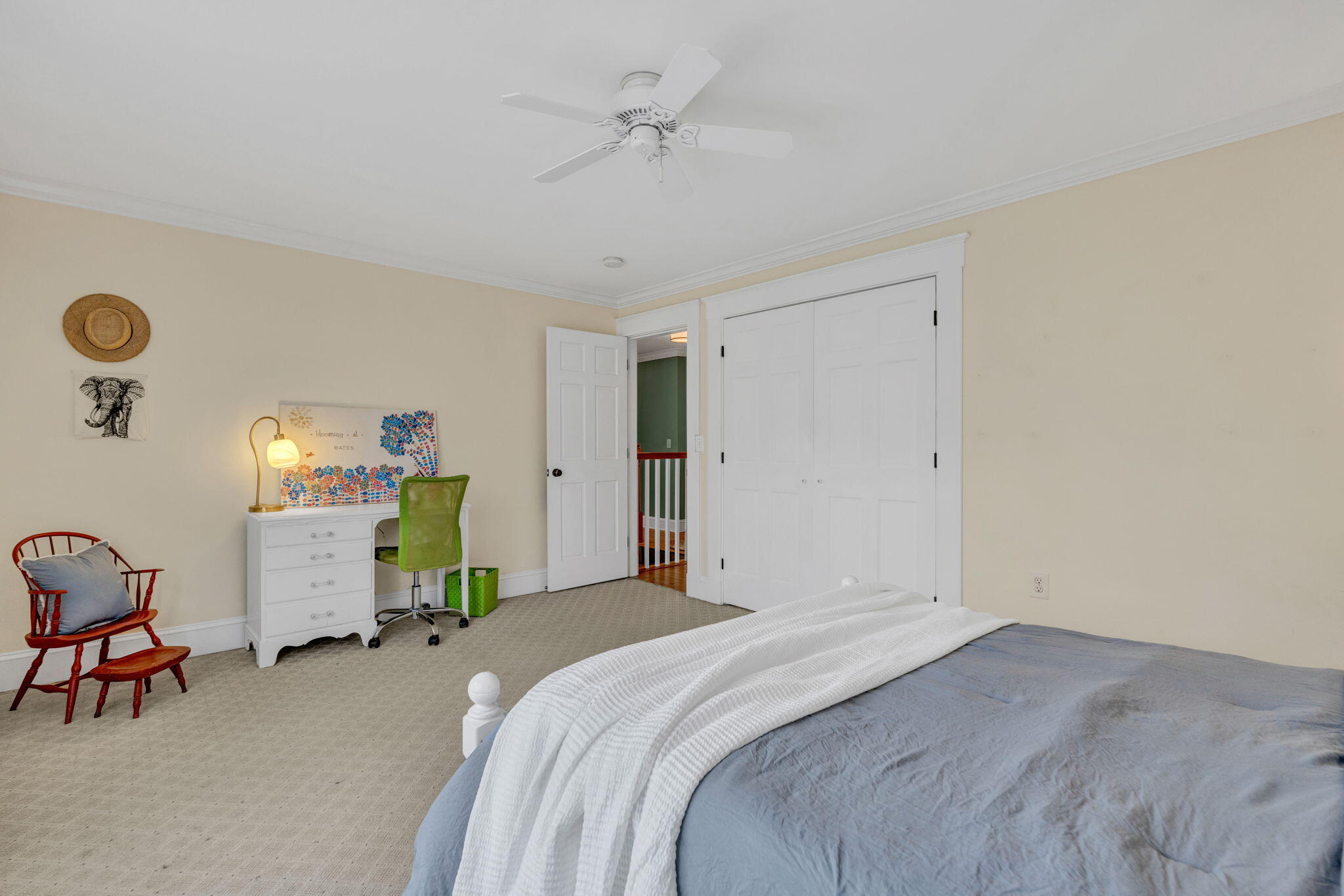 Furnished bedroom with a blue bed, green desk chair, wooden rocking chair, and white closet doors.