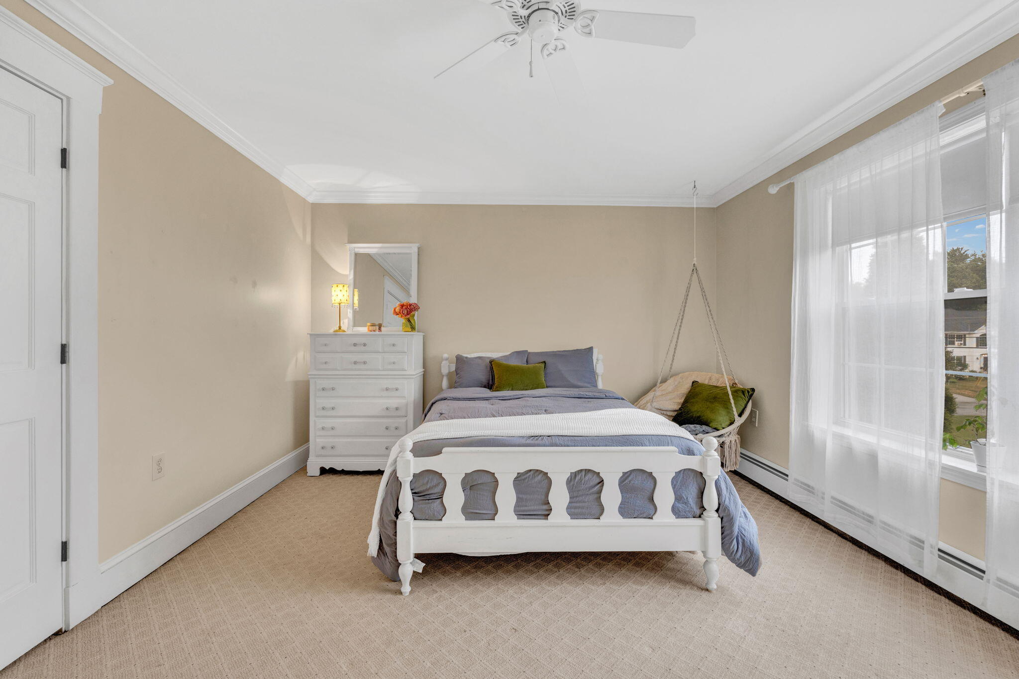 Bedroom with a white carved bed, gray bedding, and a hanging chair beside tall windows.