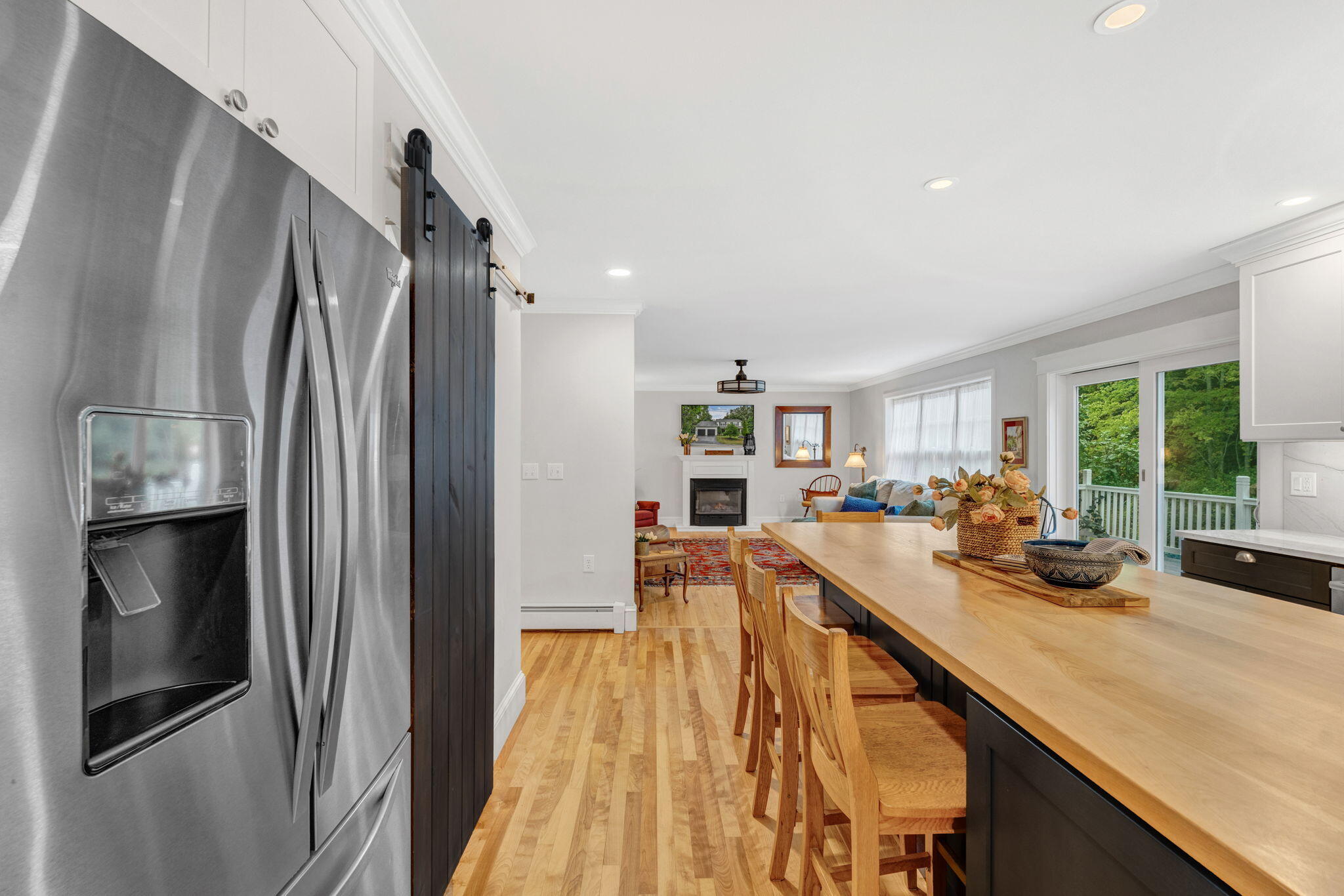 Kitchen with a long wood-topped island, stainless refrigerator, and open view into the living room.
