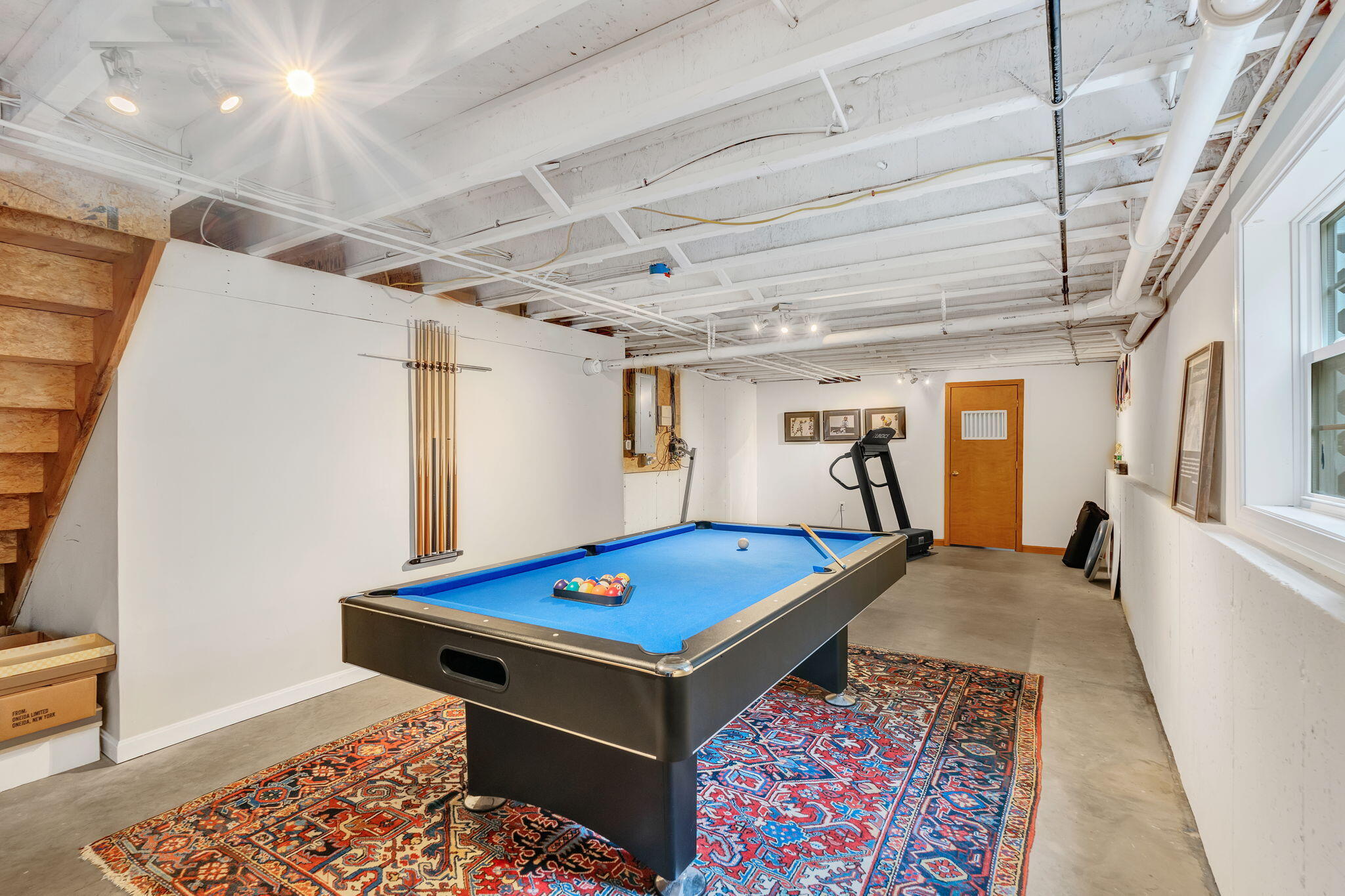 Basement game room with a blue pool table, patterned rugs, and treadmill.