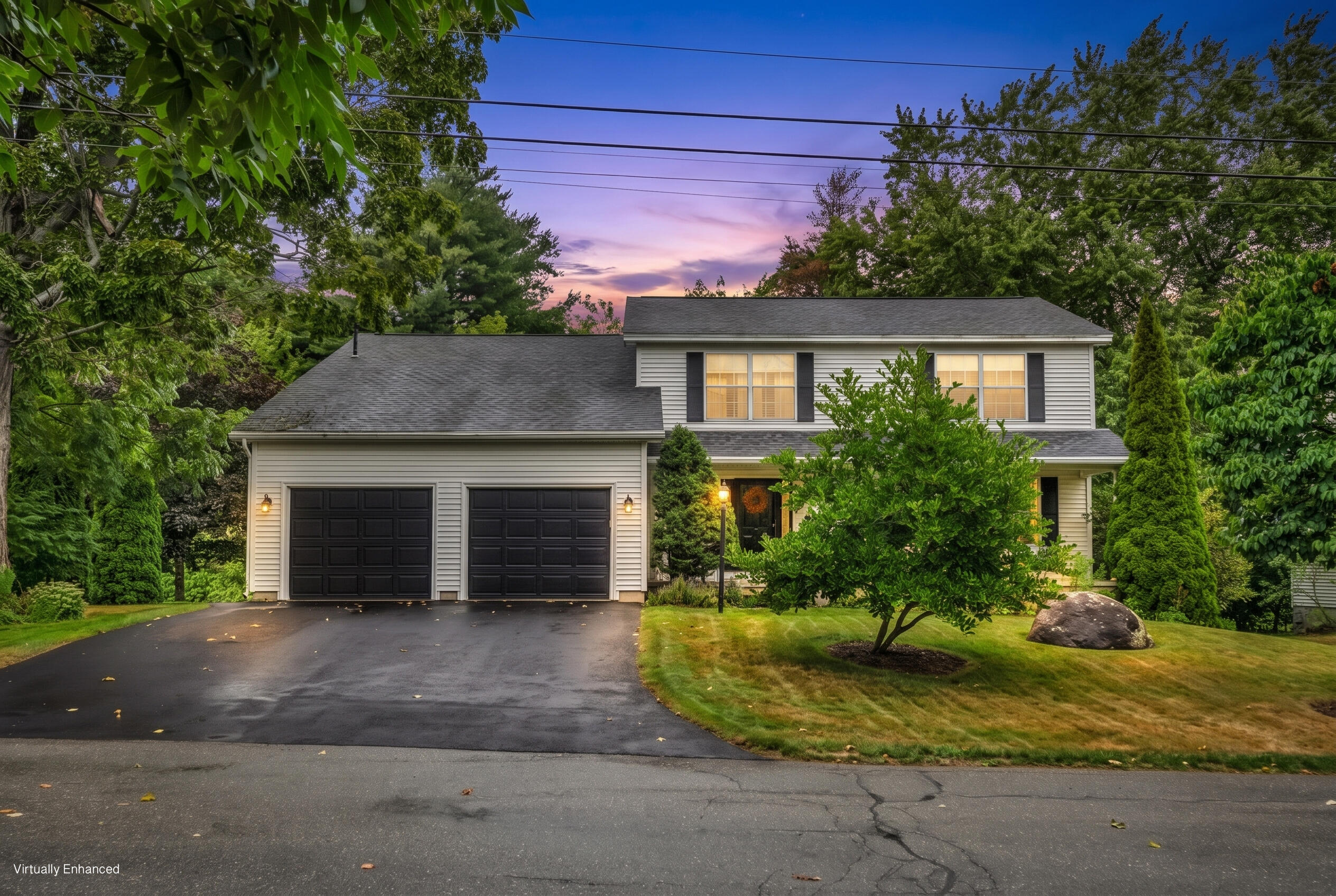 Two-story home with twin garage doors, landscaped yard, and glowing windows at dusk.