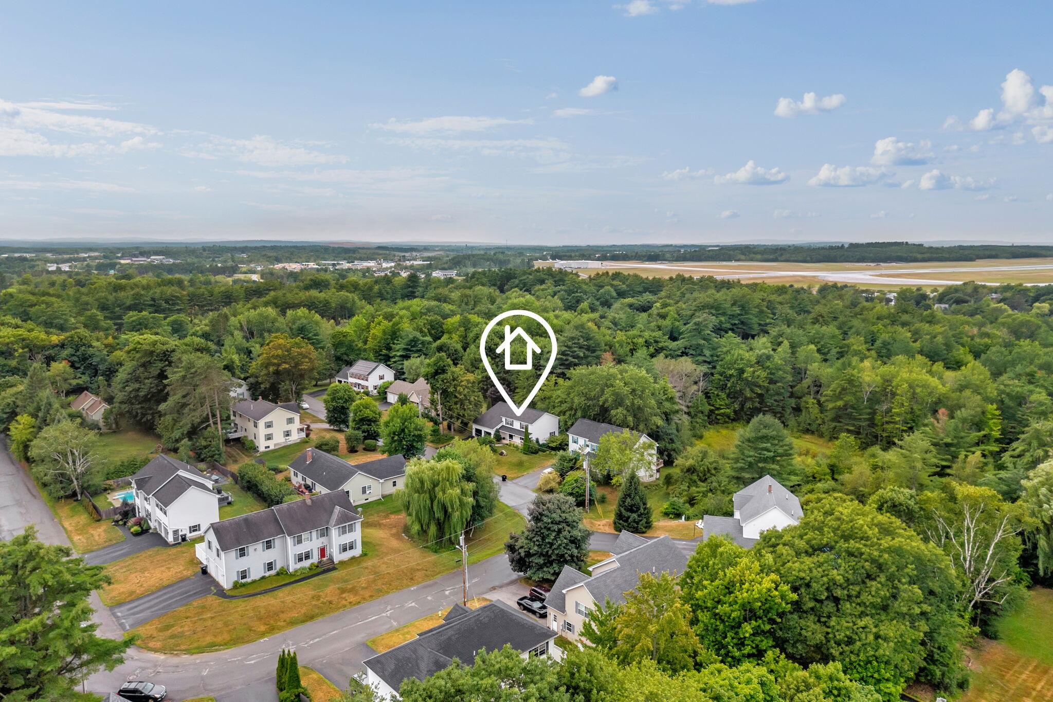 Aerial view of 63 Fairways, marked among tree-lined homes with an airport runway in the distance.