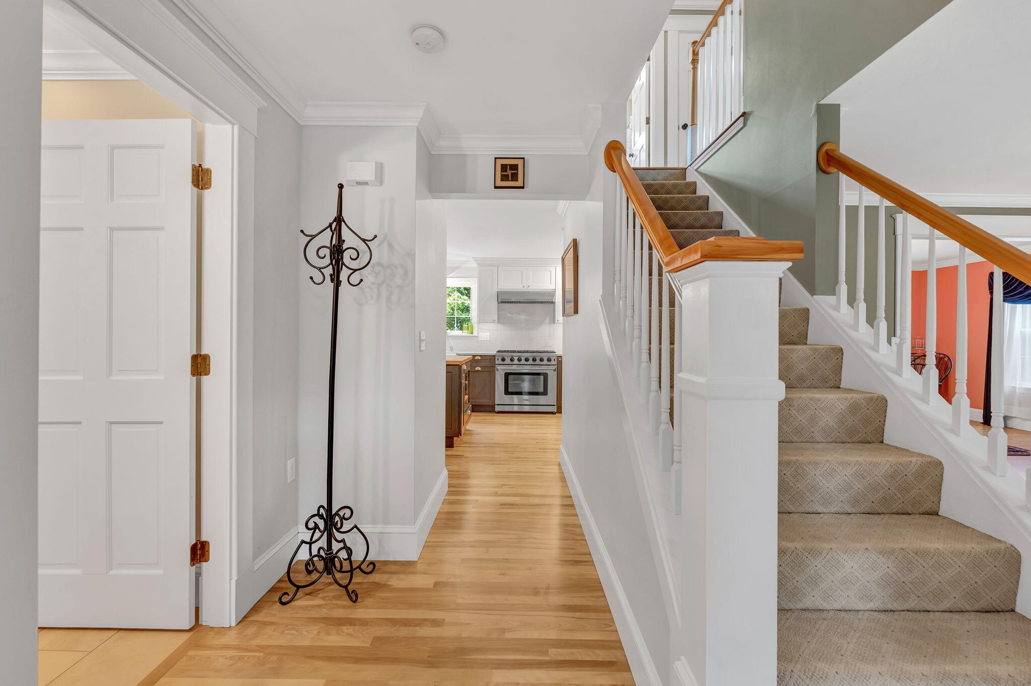 Bright hallway with hardwood floors, a carpeted staircase, and a view into the kitchen.