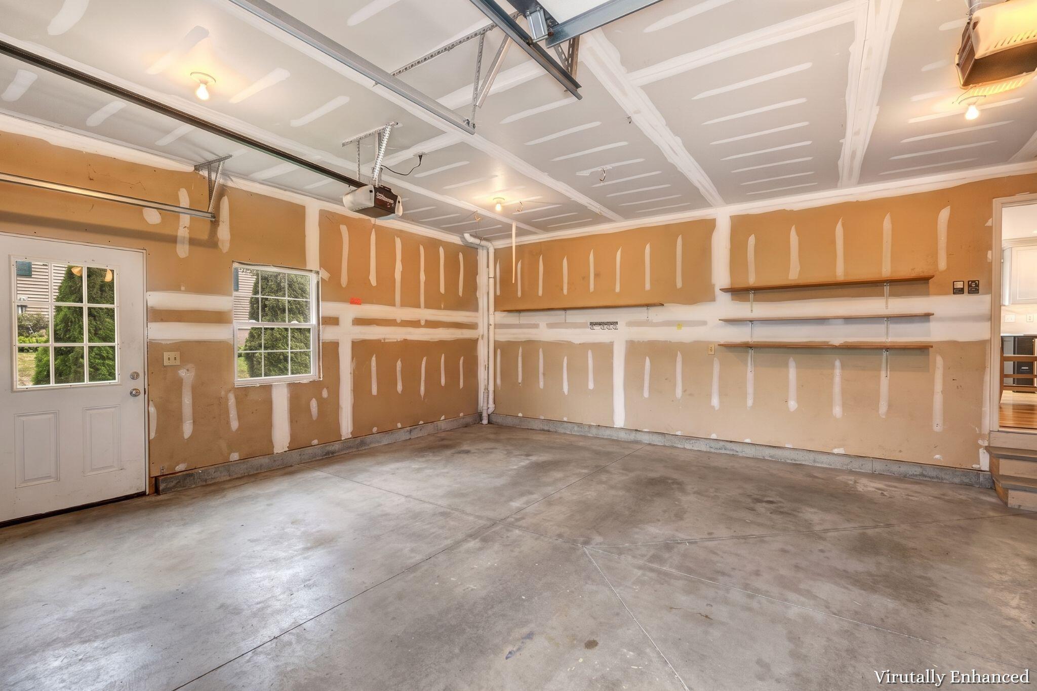 Unfinished garage with concrete floor, wall shelves, windows, and exposed overhead door tracks.