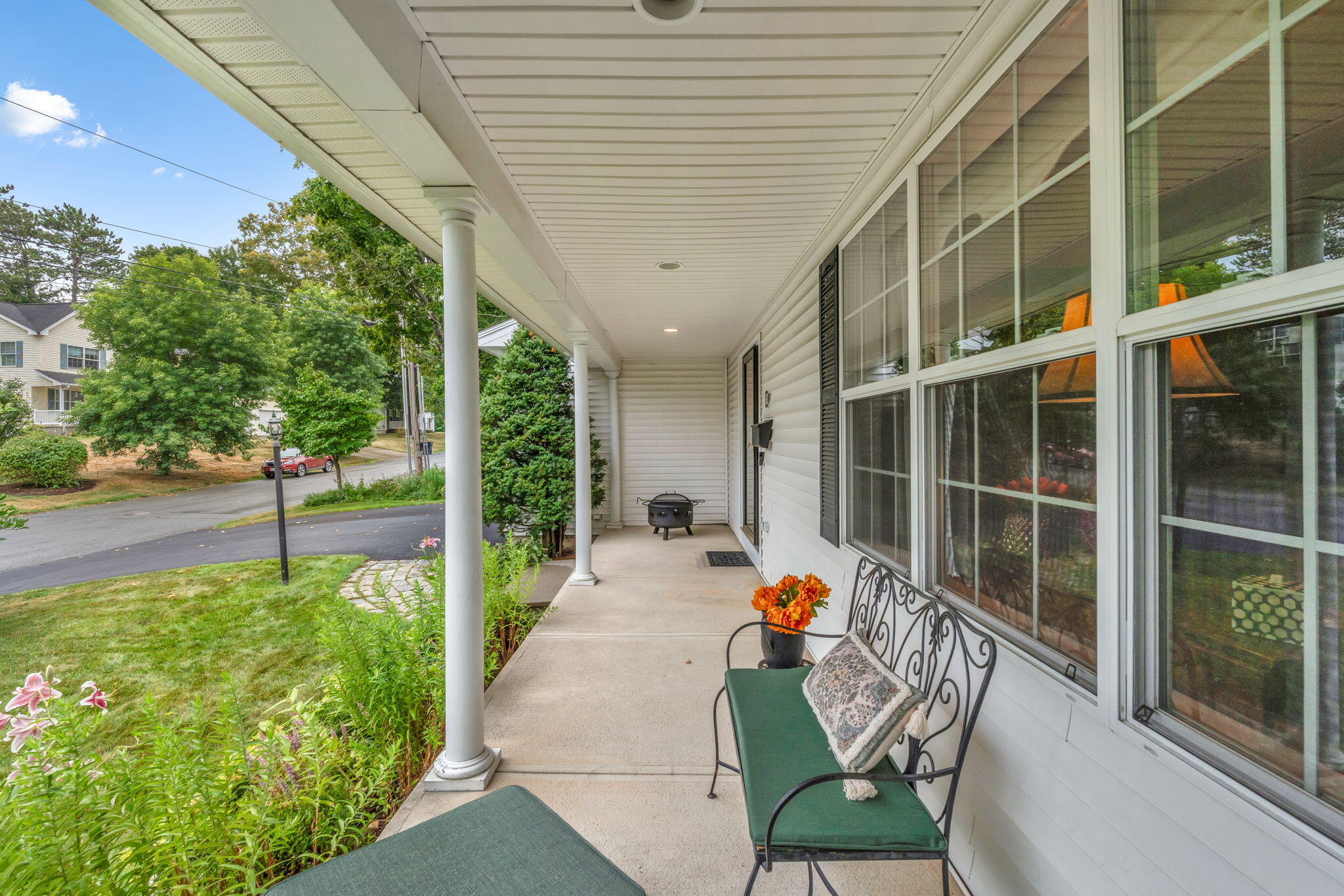 Covered front porch with white columns, a green bench, orange flowers, and a view of the street.