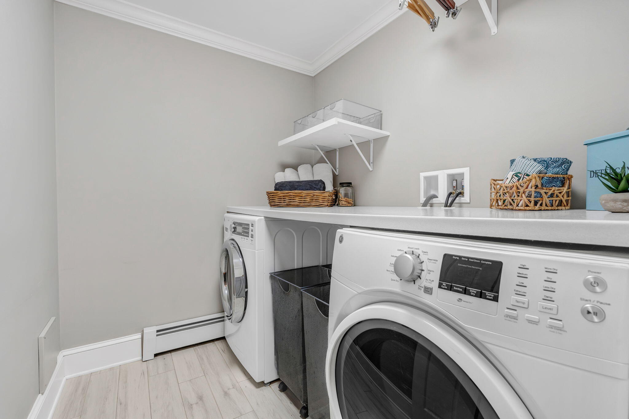 Laundry room with front-loading washer and dryer, countertop, baskets, and wall shelf.