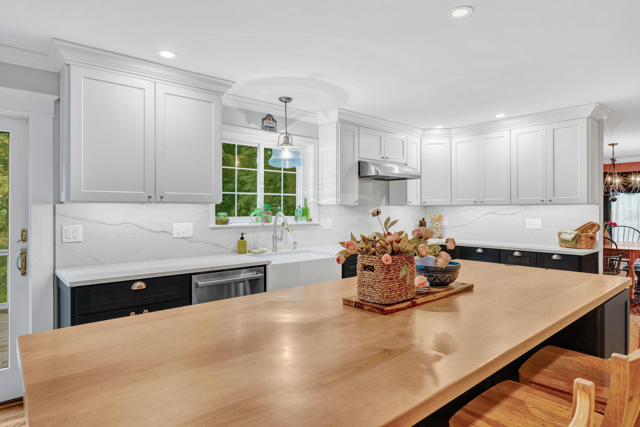 Kitchen with white cabinets, marble-look backsplash, and a large wood island with stools.