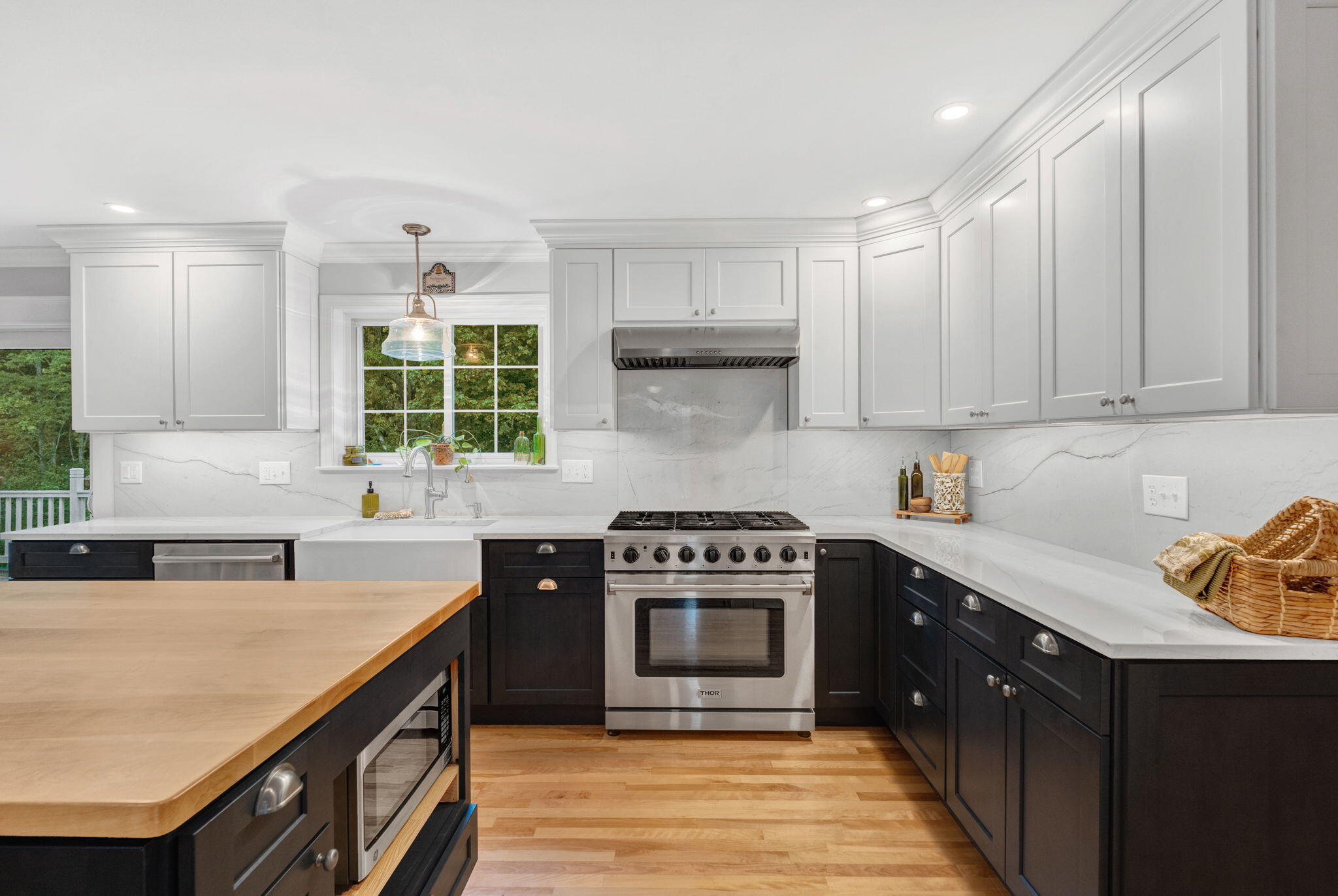 Kitchen with white upper cabinets, dark lower cabinets, a stainless steel range, and a wood-topped island.