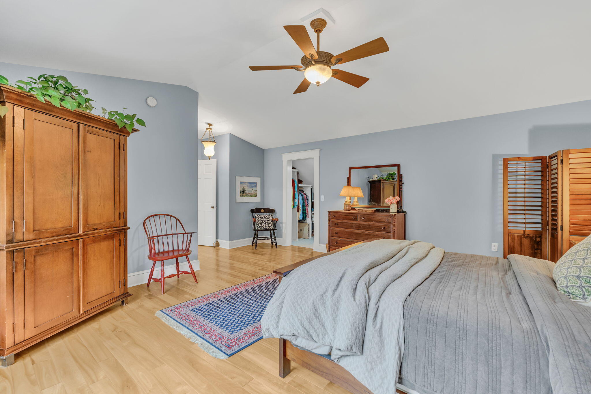 Bedroom with gray bedding, hardwood floors, and a large wooden armoire.